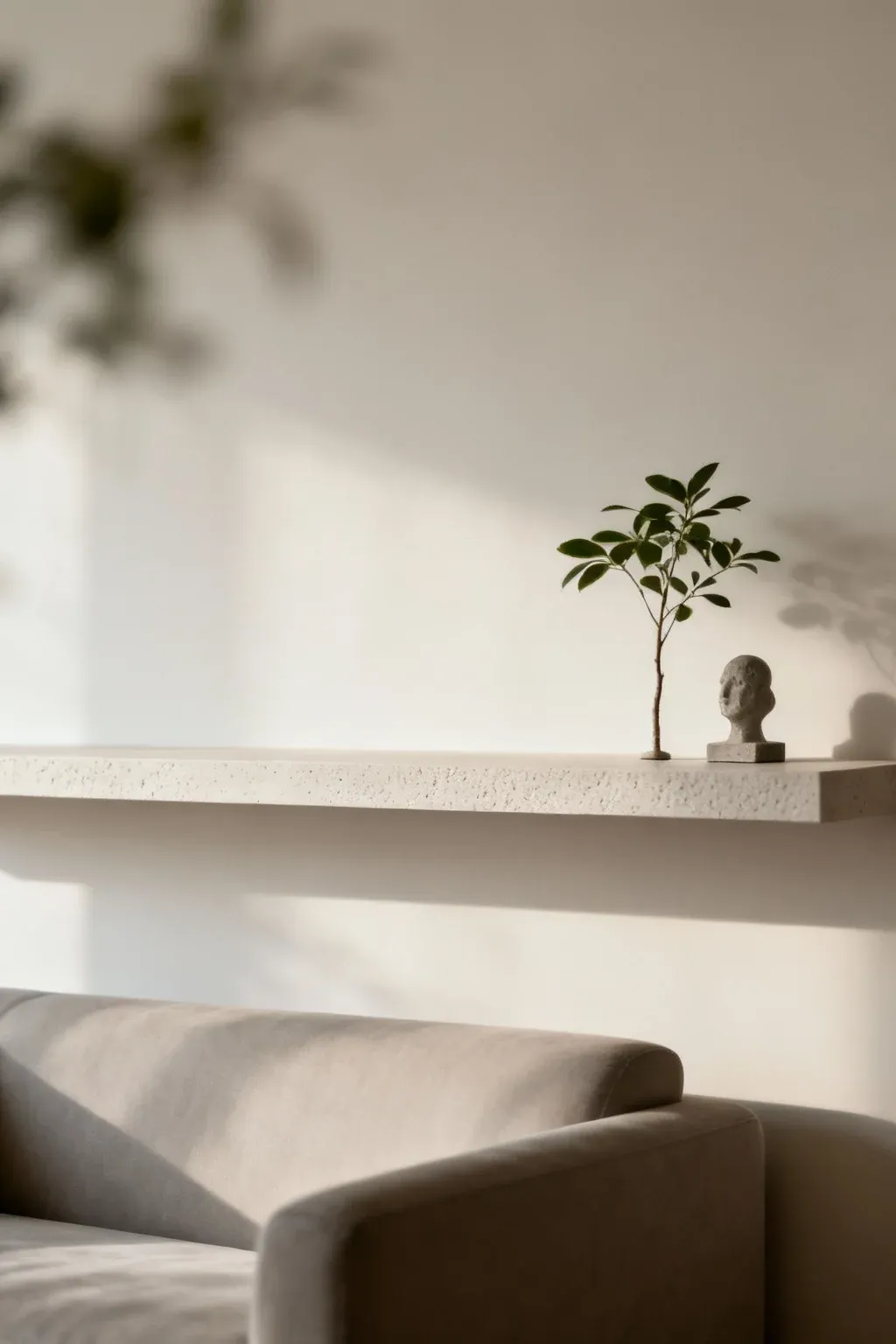 Minimalist shelf above a couch displaying a single plant and sculpture.