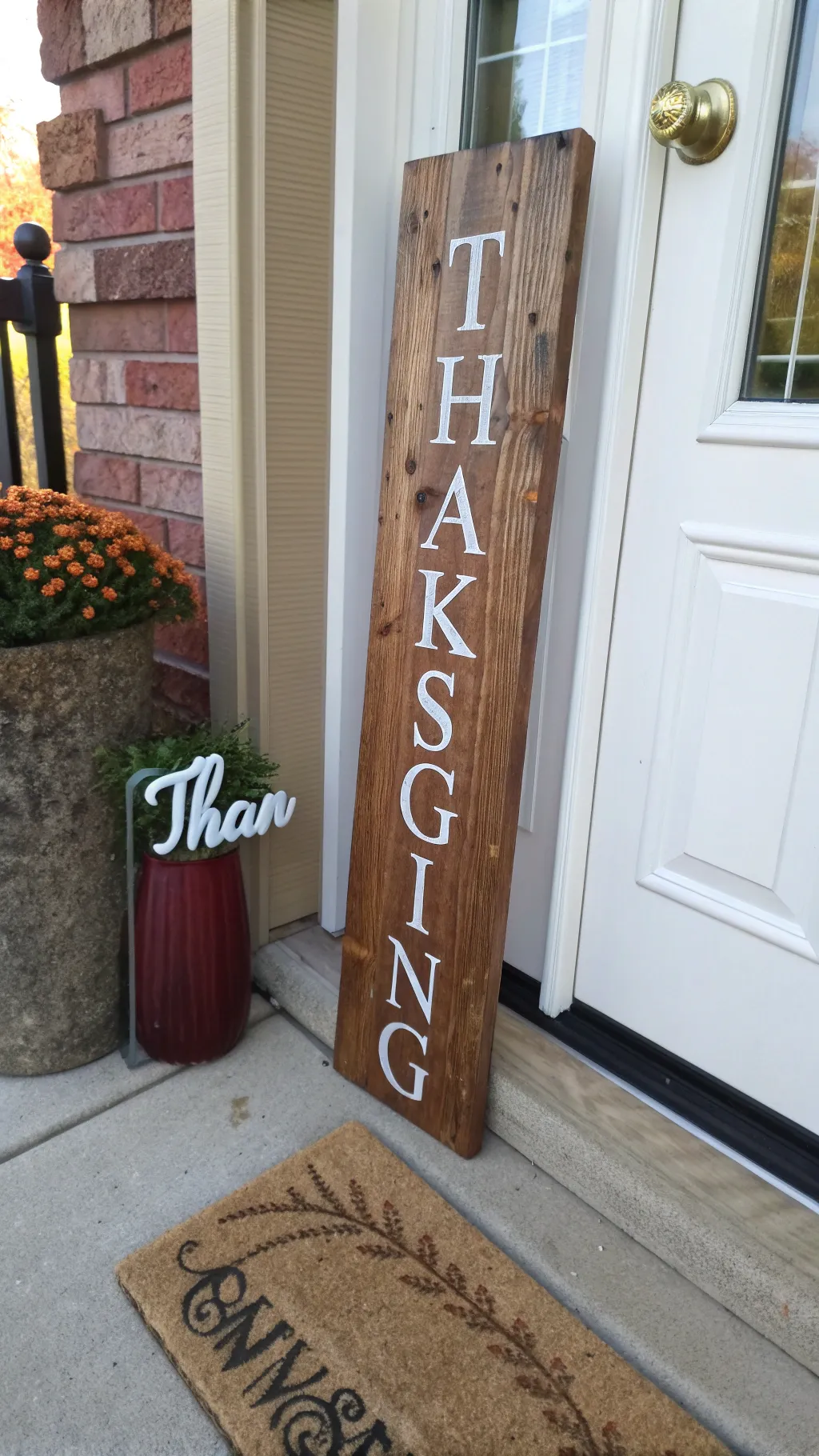 Rustic wooden sign with a painted thankful message placed beside a warmly decorated autumn porch doorway.