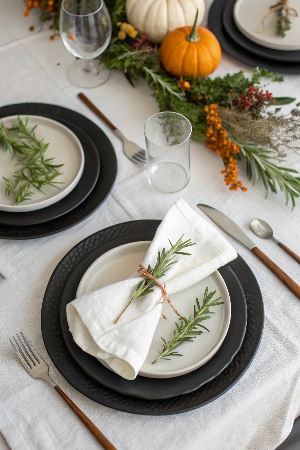 Overhead view of matte black plates with white linens and rosemary sprigs on a modern Thanksgiving table.