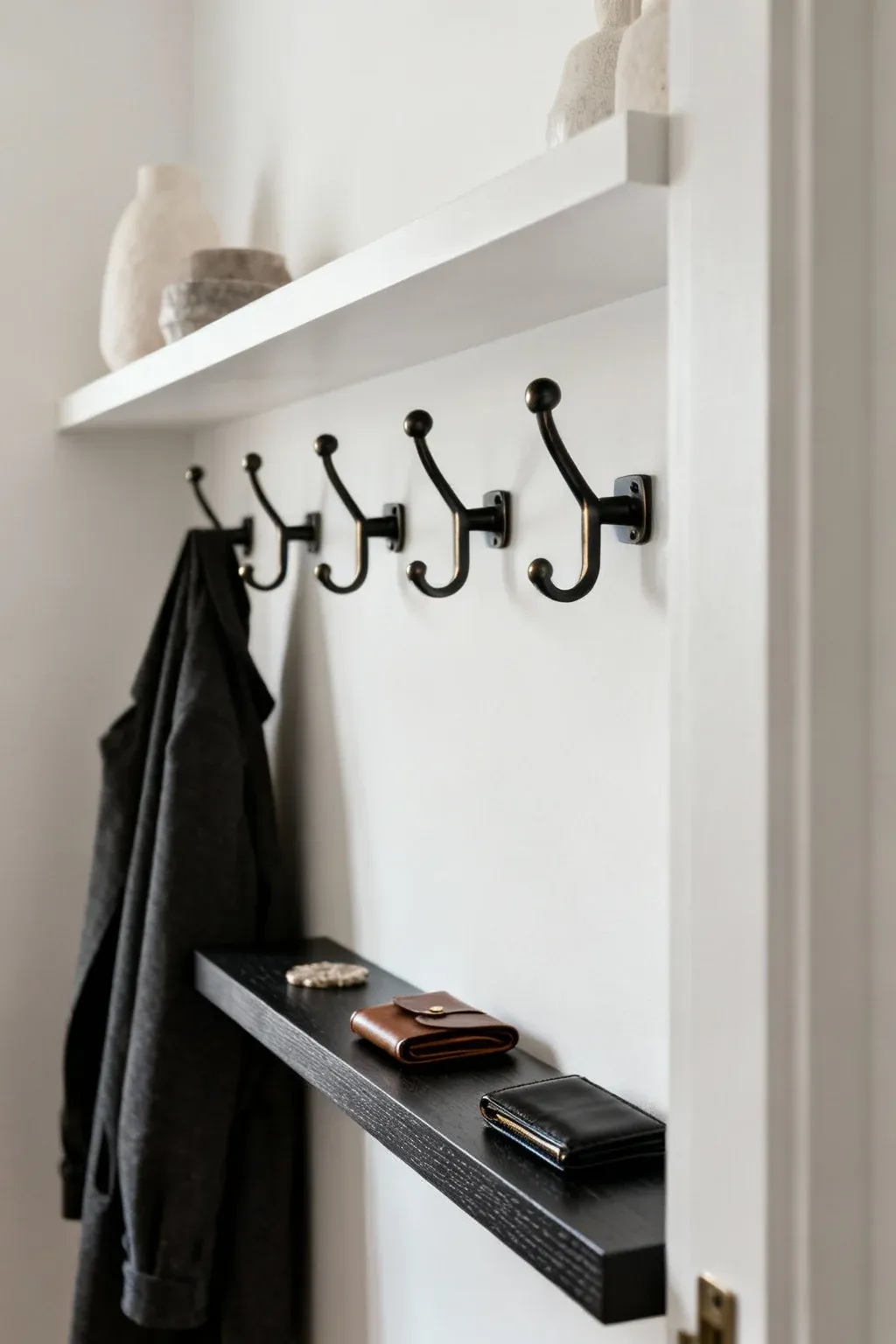 Floating wall ledge and hooks holding coats and decor in a small entryway.