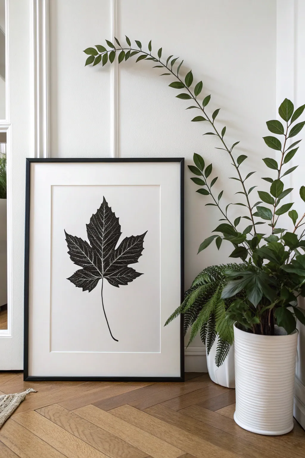 Minimalist wall art depicting a black leaf silhouette on a white background in soft daylight.