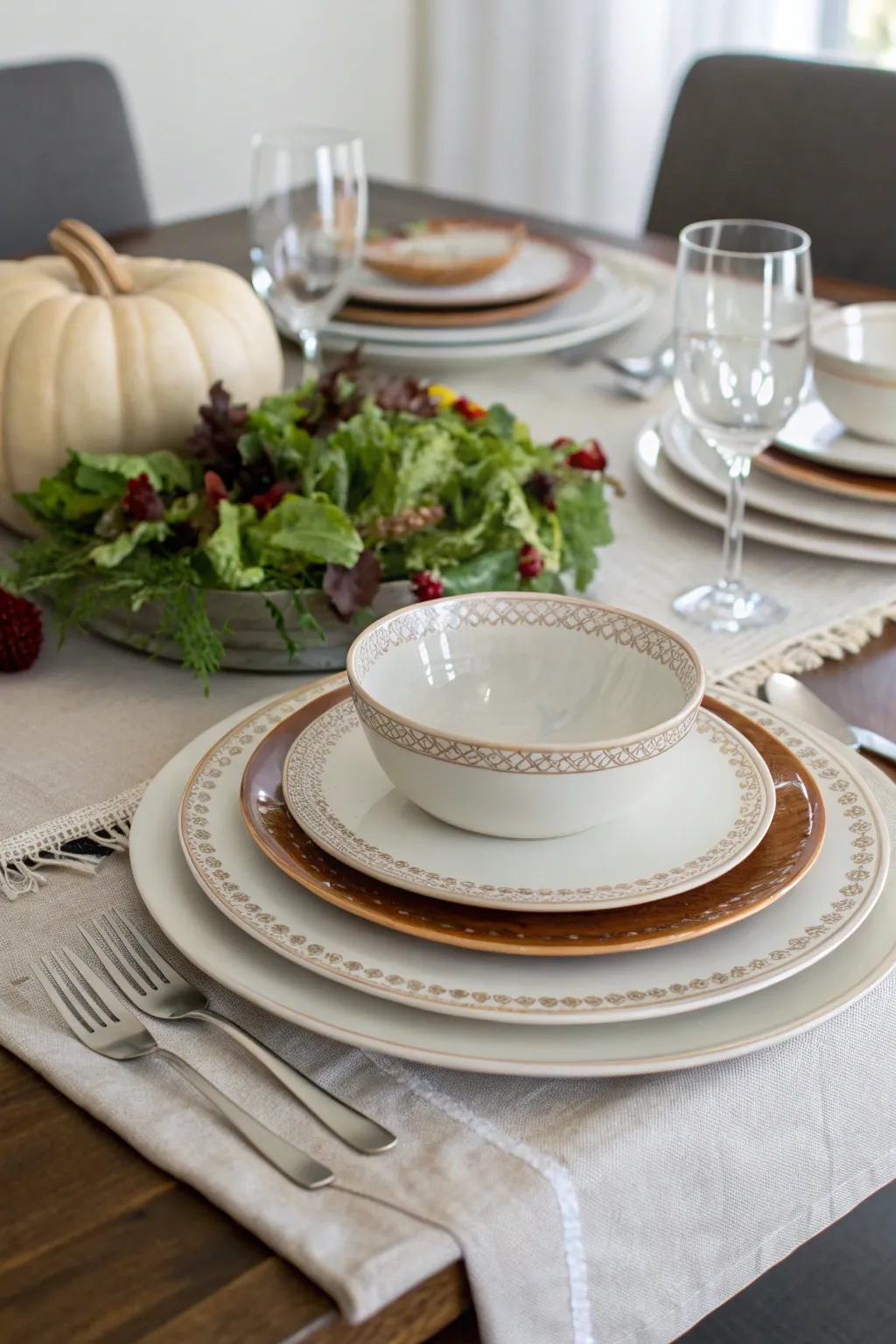 Layered plates and napkin in warm neutral tones arranged neatly for a Thanksgiving table.