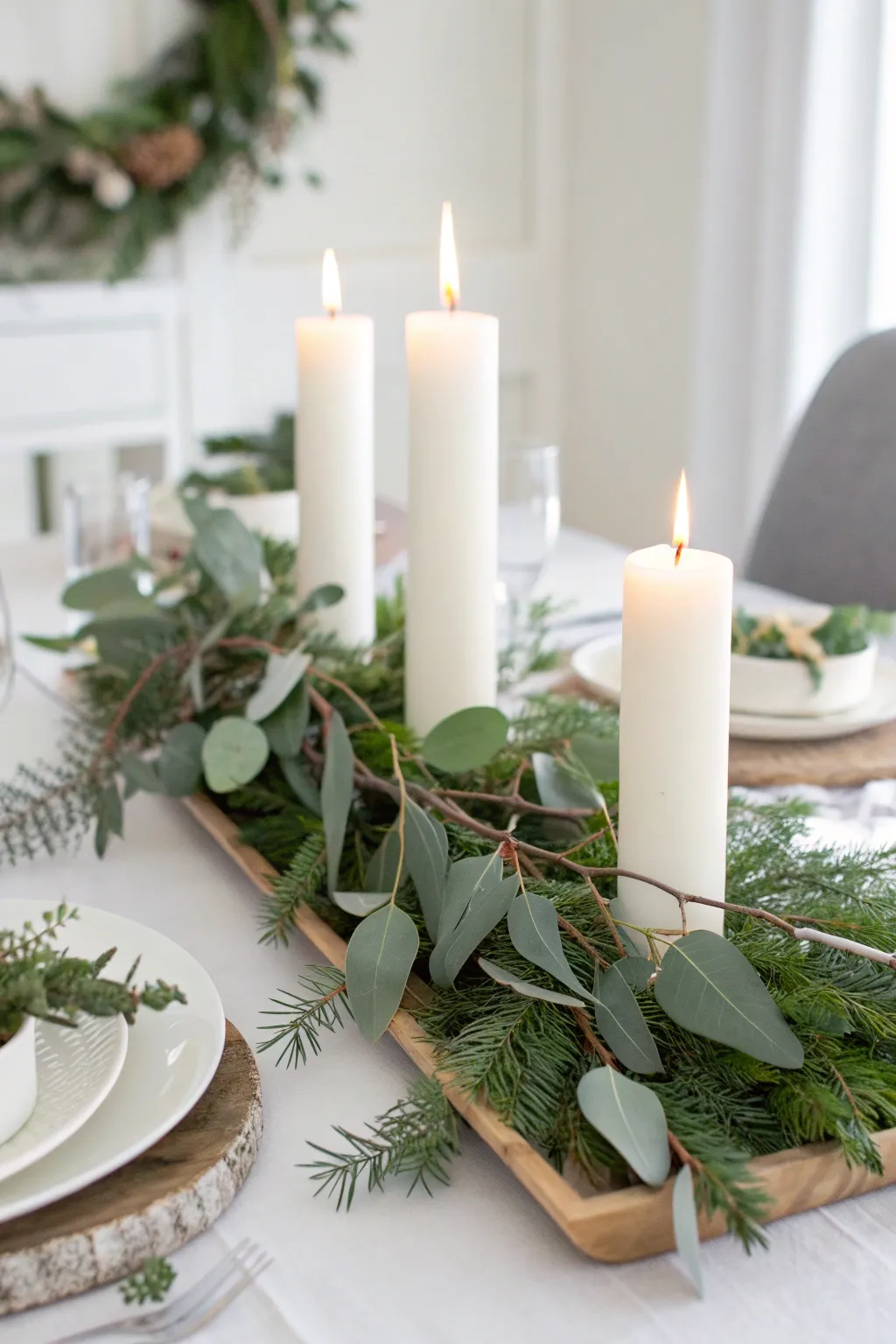 Simple holiday table centerpiece with white candles nestled among fresh eucalyptus branches.