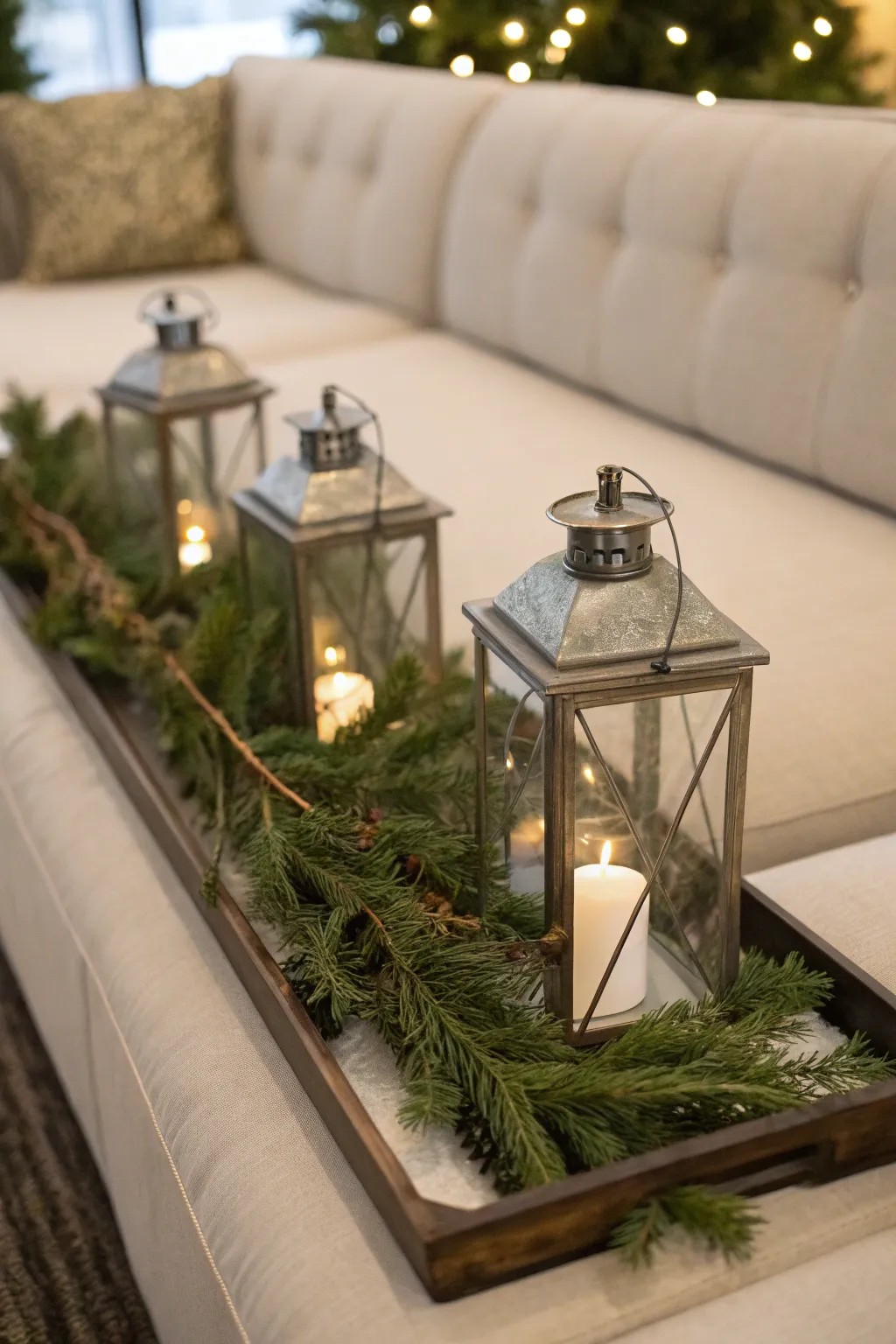 Sofa table tray with lanterns and pine garland creating soft festive illumination.