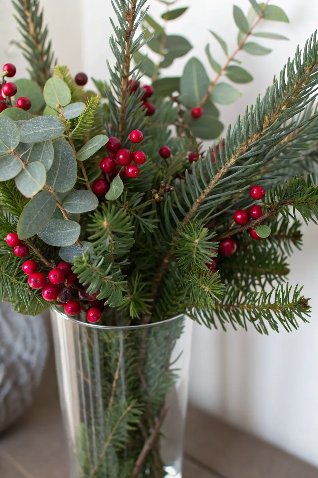 Glass vase with fresh pine branches and cranberries for a simple Christmas accent.