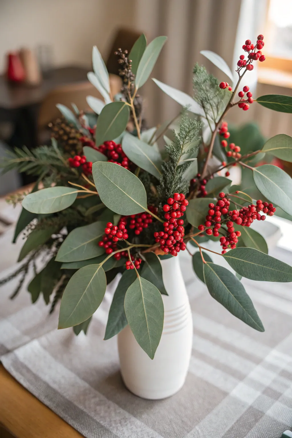 Low floral Christmas arrangement with eucalyptus leaves and clusters of red berries.
