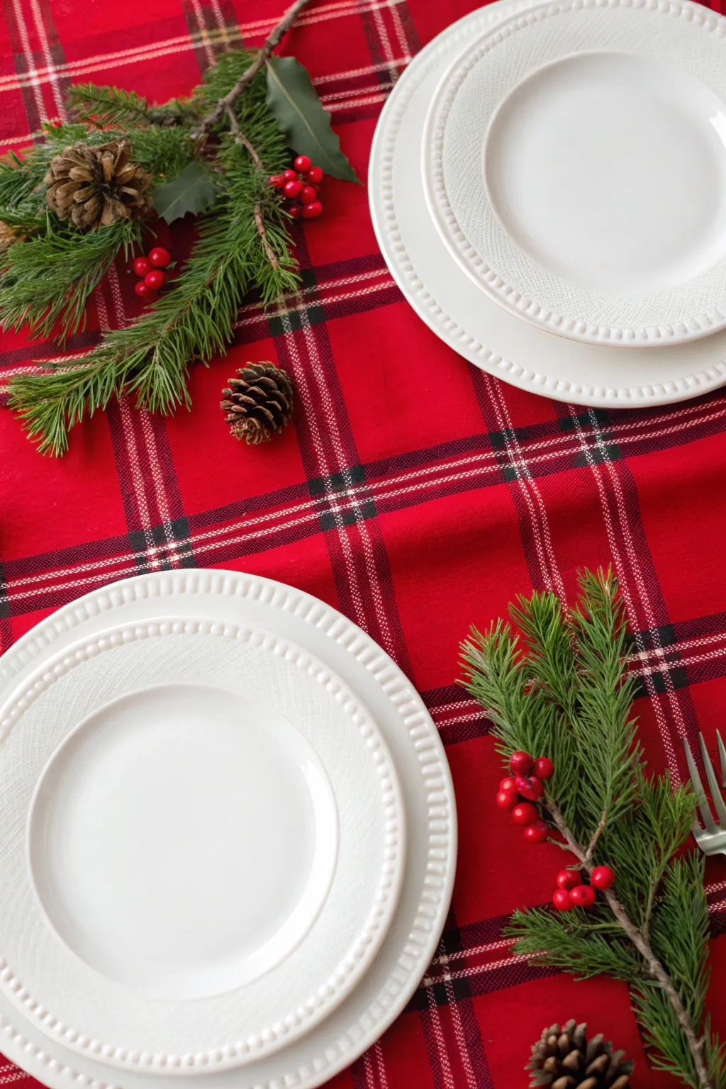White plates set on a red plaid tablecloth with pine sprigs for a festive casual meal