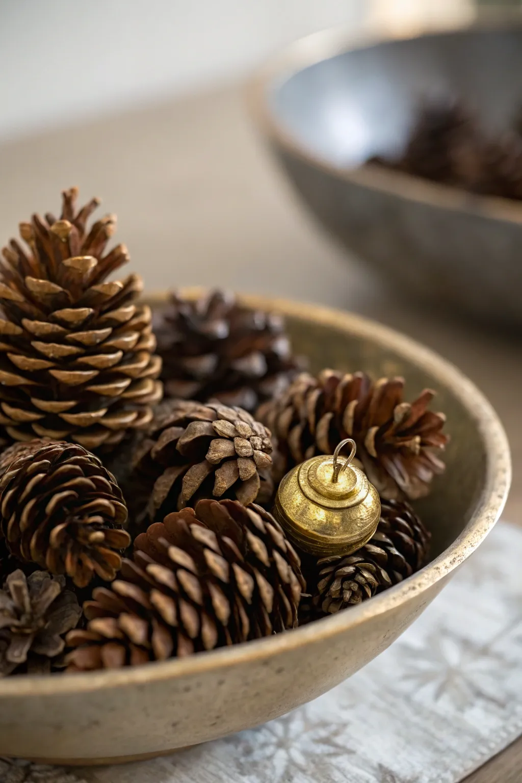 A bowl filled with pinecones next to a small brass accent piece on a winter table.