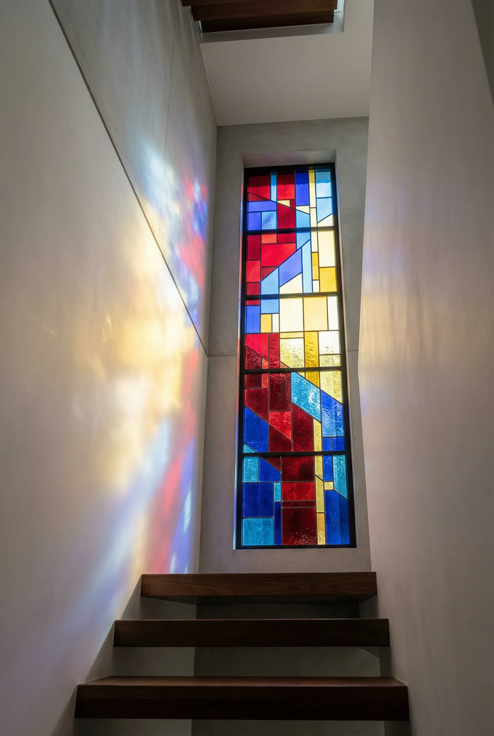 Bold modern stained glass panel casting vibrant colors along a clean stairwell wall.