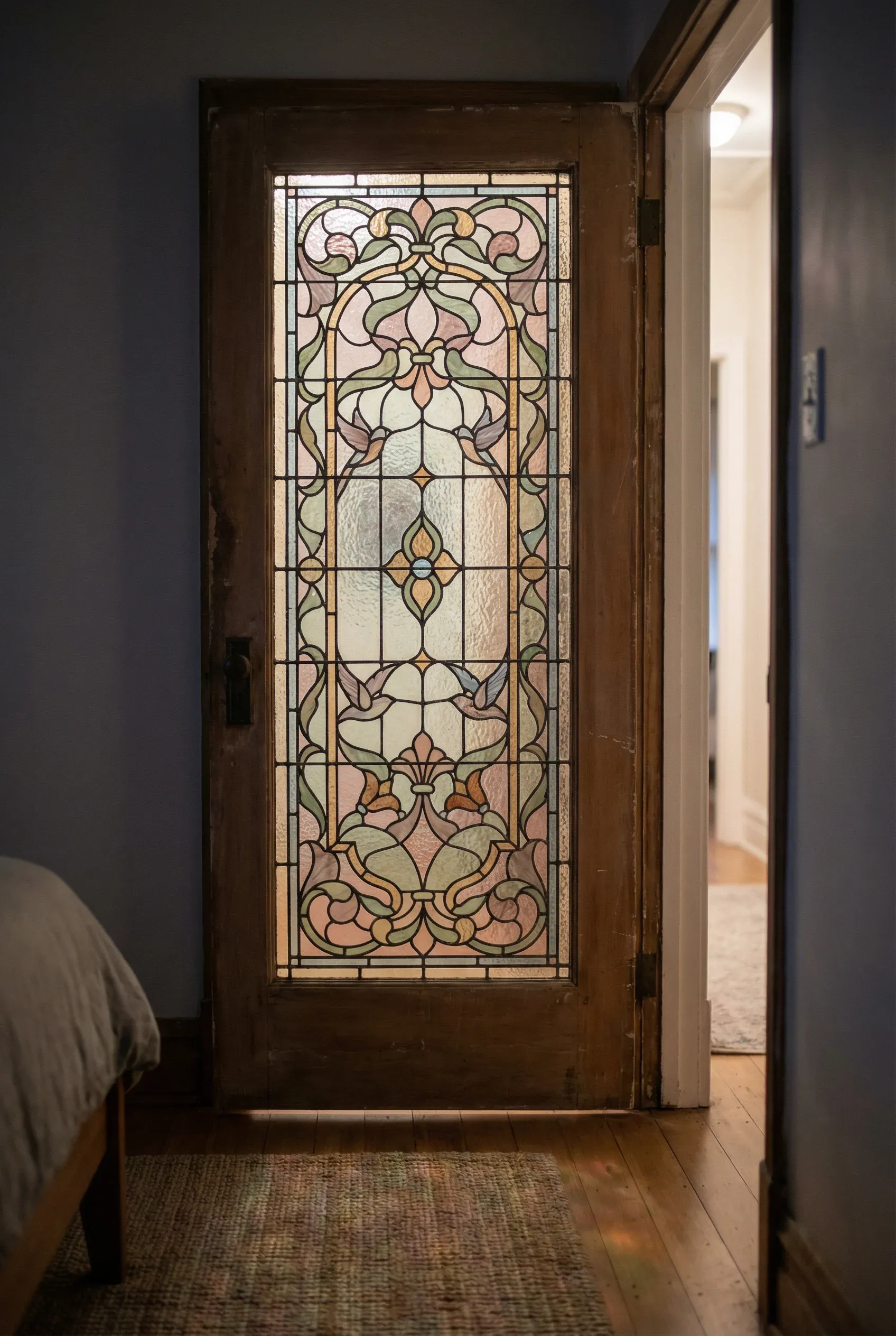 Restored antique stained glass inset glowing softly within a quiet bedroom door.