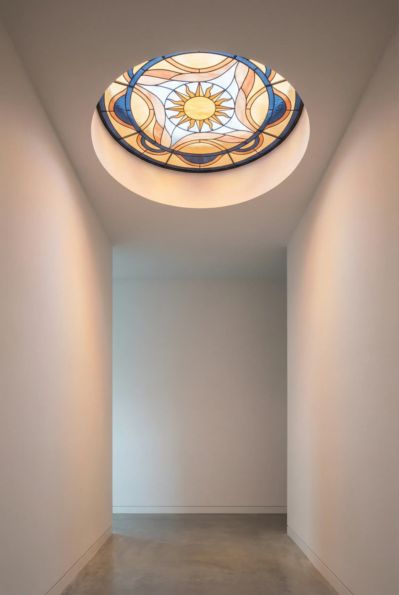 Custom stained glass skylight casting warm colored light into a minimalist hallway.