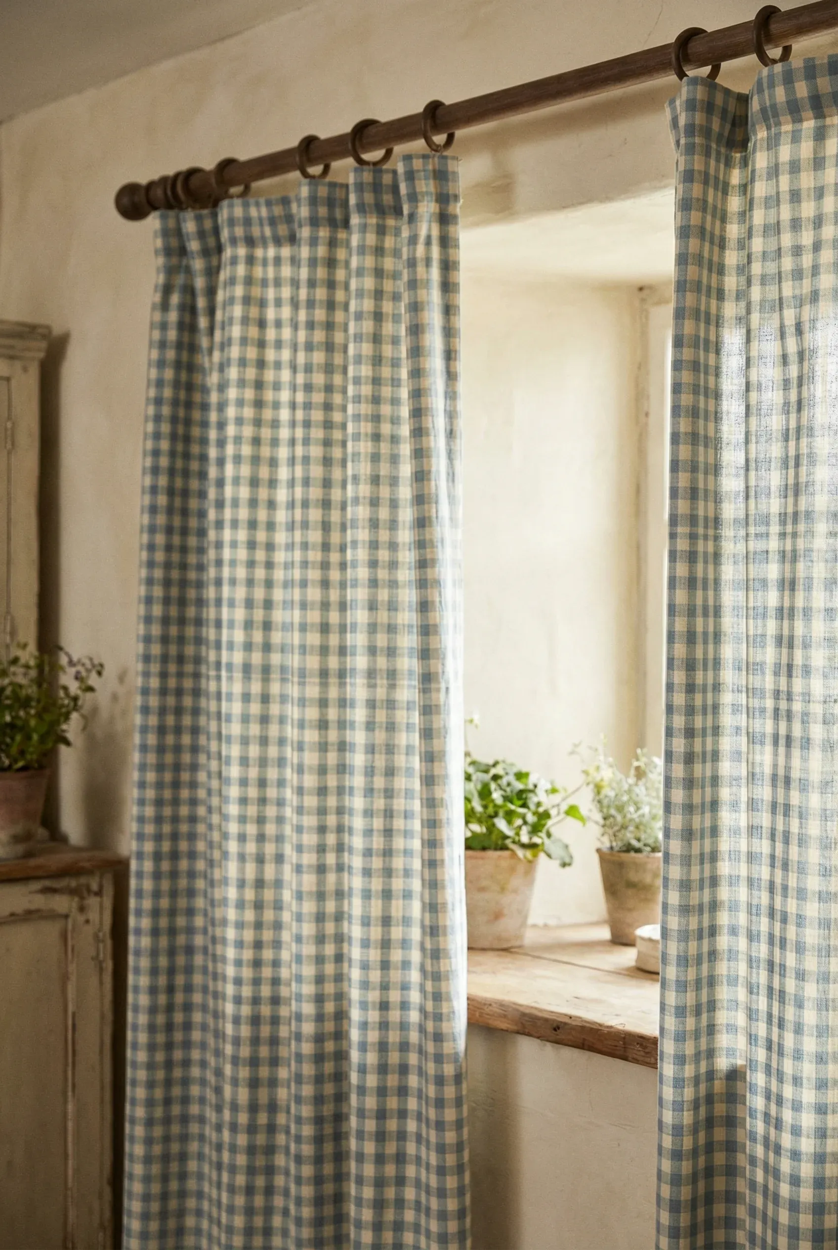 Soft checked cotton curtains hanging from a wooden rod in a country cottage interior.