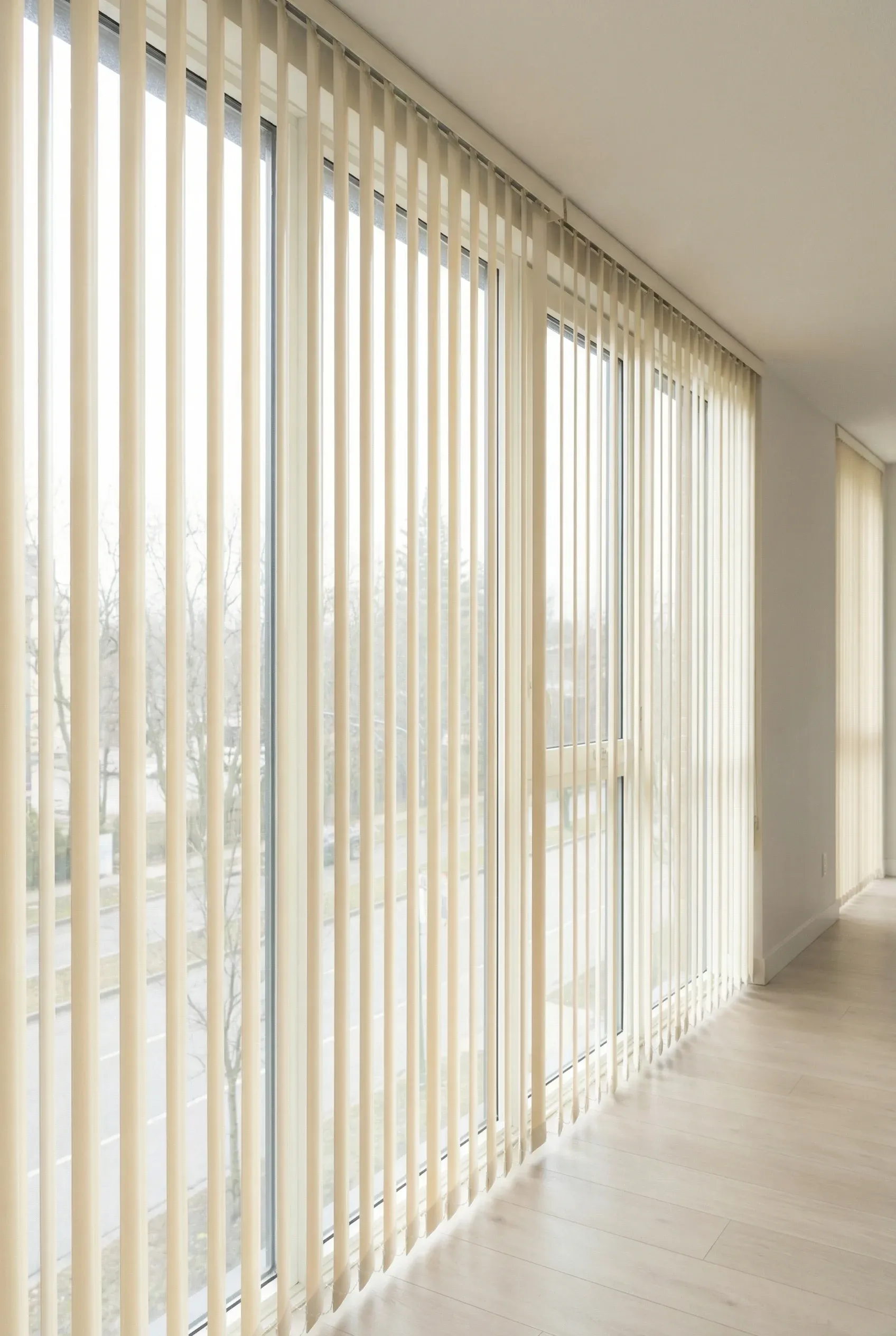 Ivory vertical blinds with a soft sheen filtering daylight through tall windows.