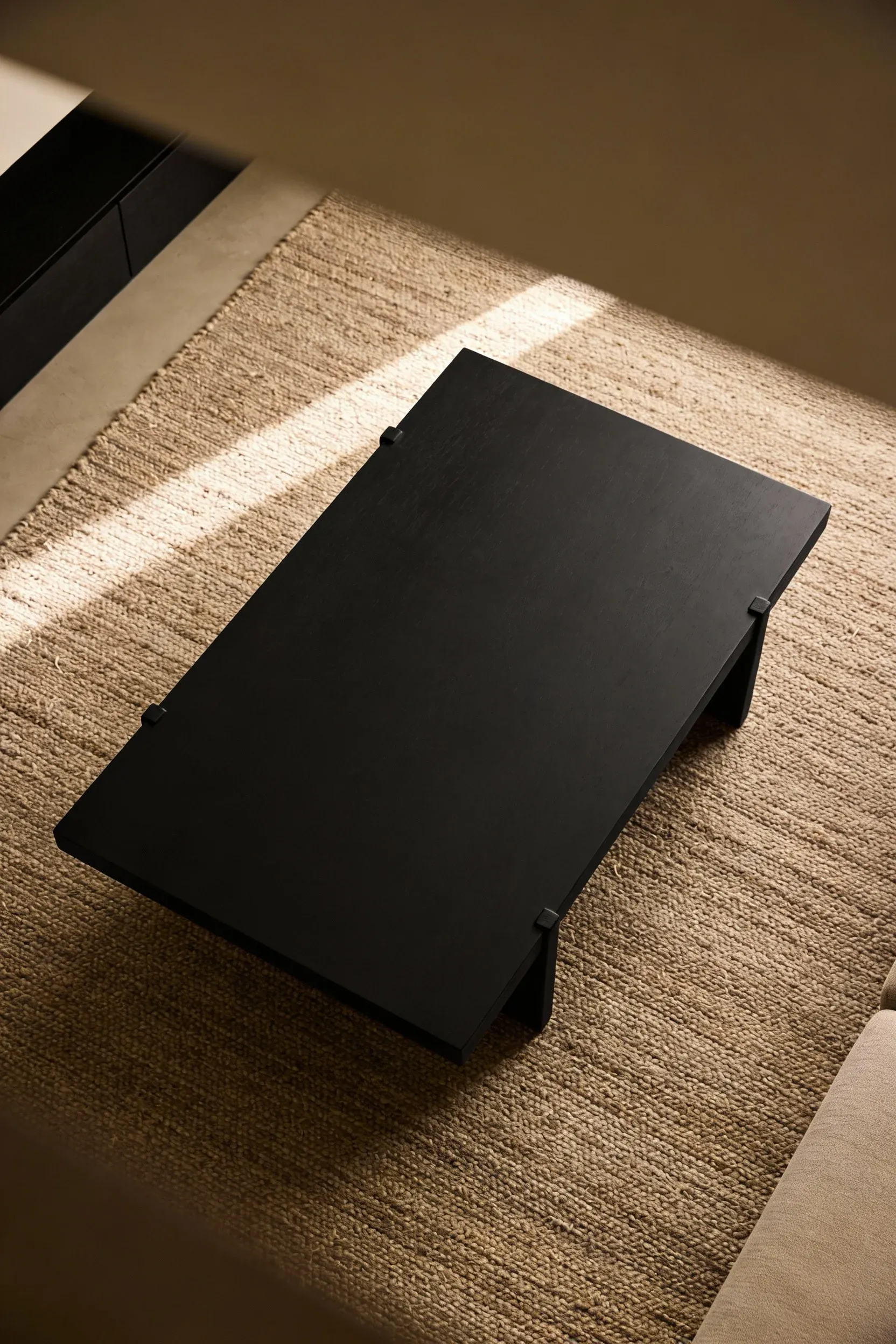 Matte black coffee table sitting on a textured taupe rug in a neutral living space.