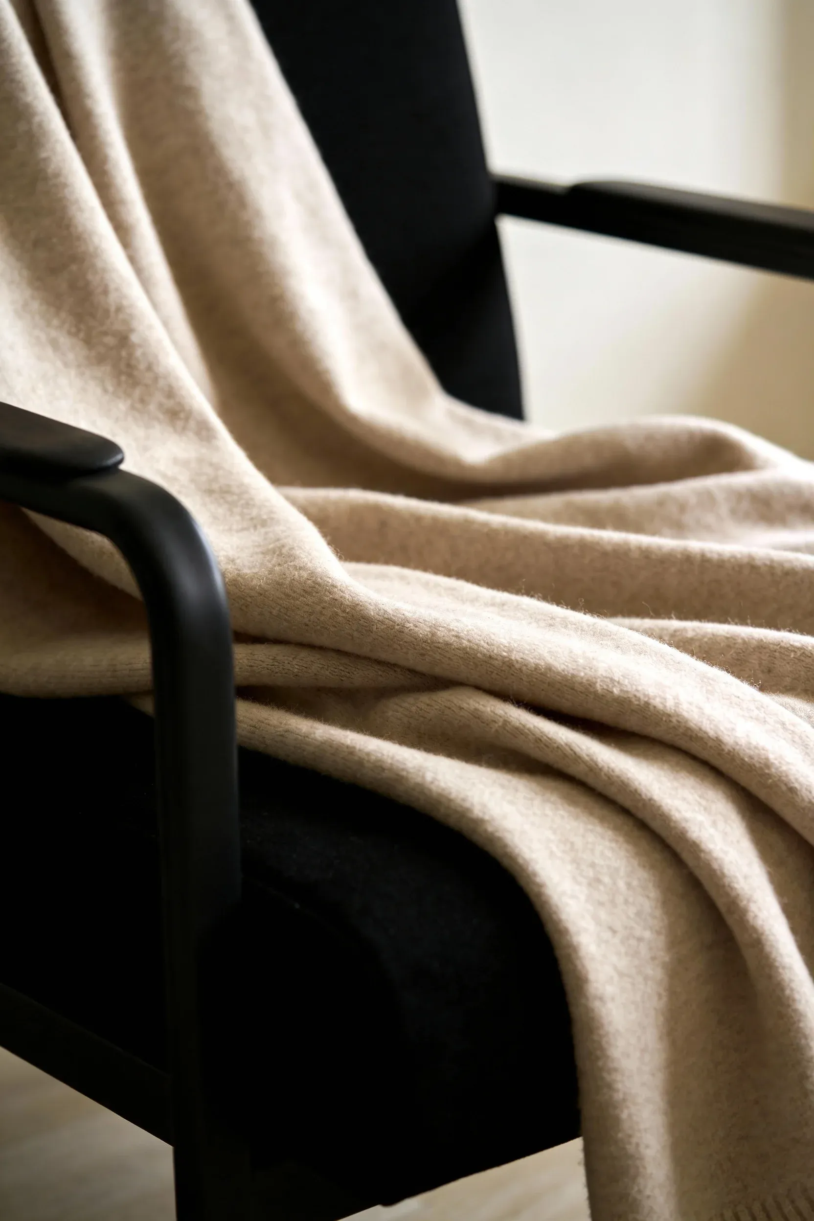 Soft beige throw blanket draped over a black armchair in a cozy living room.