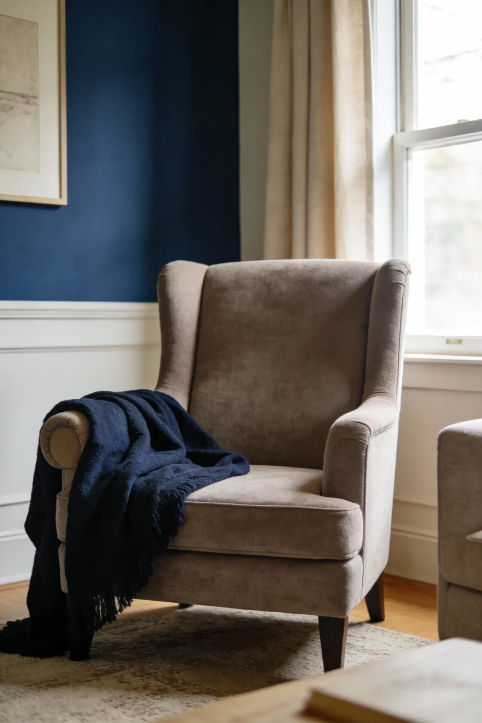 A taupe fabric accent chair in a navy blue and beige living room with a throw blanket.