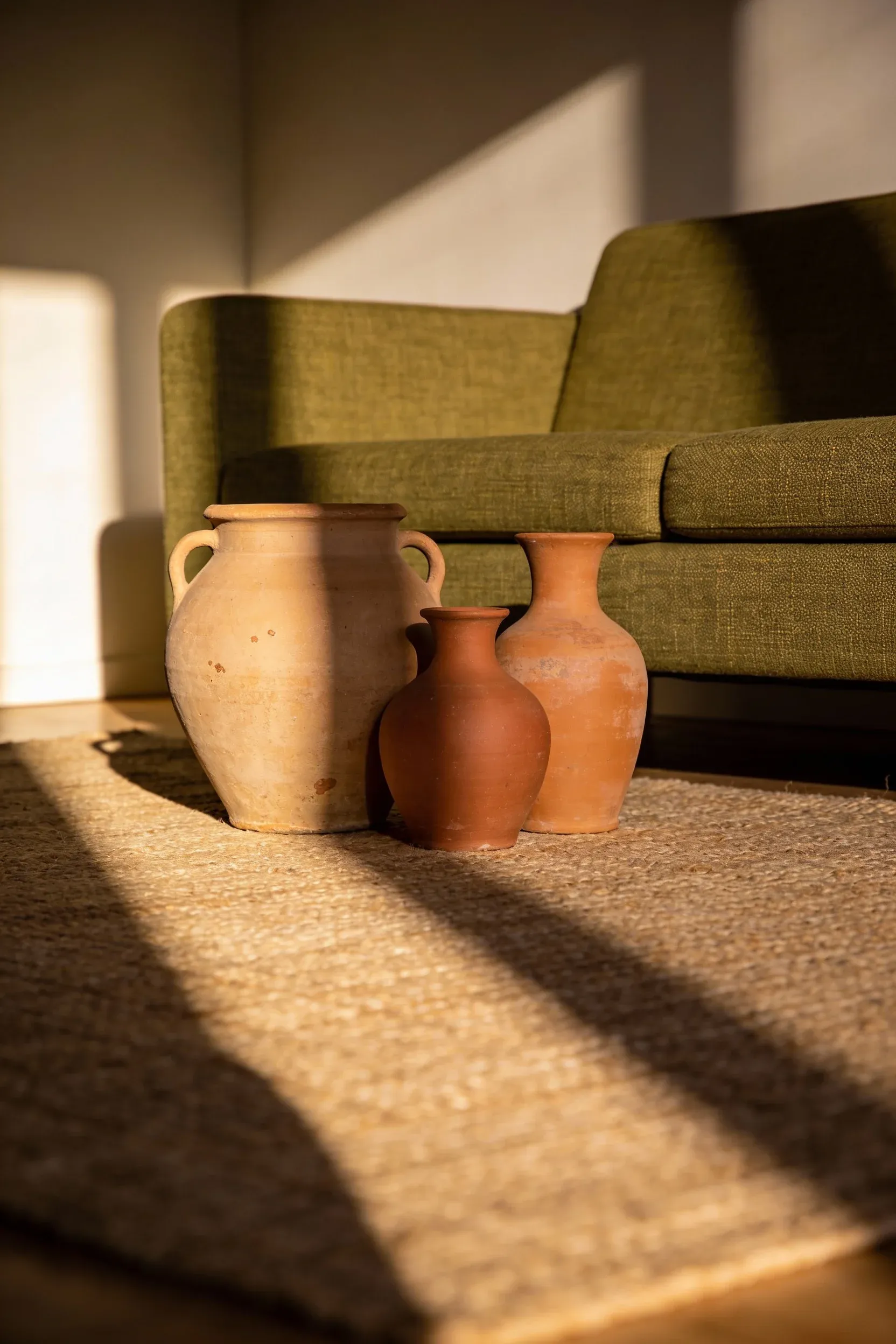 Olive green couch with warm terra-cotta pottery accents in a softly lit living room.