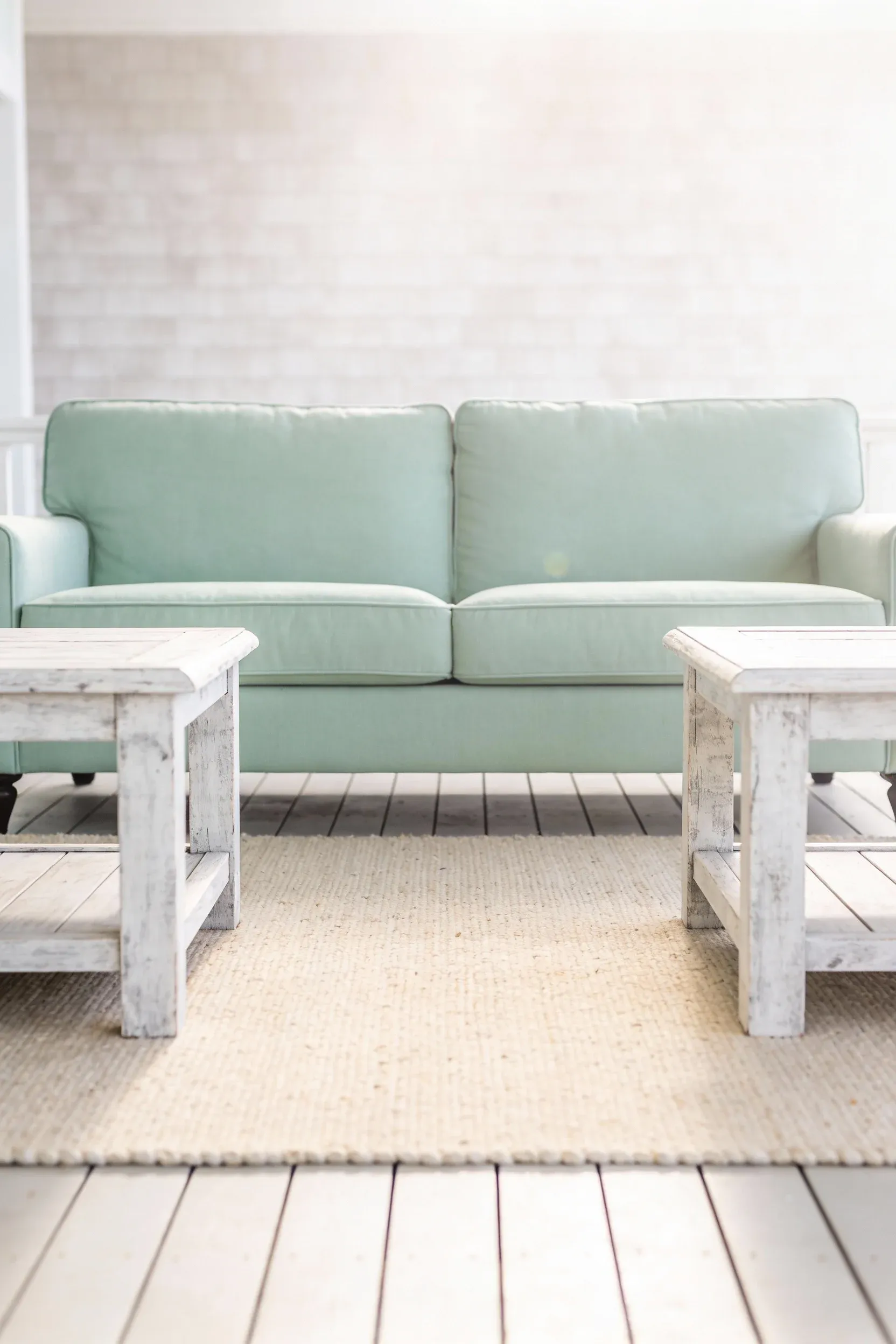 Light green sofa paired with soft whitewashed side tables in a bright coastal-style living room.