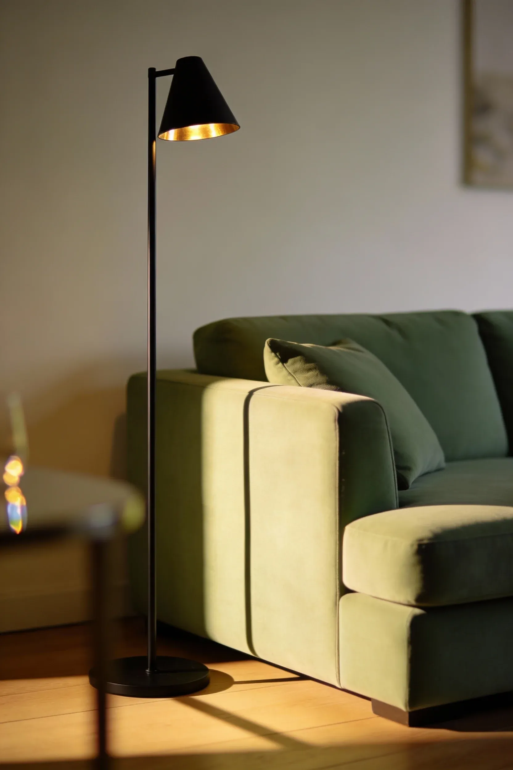 A light green couch paired with a slim black metal lamp in warm natural lighting.