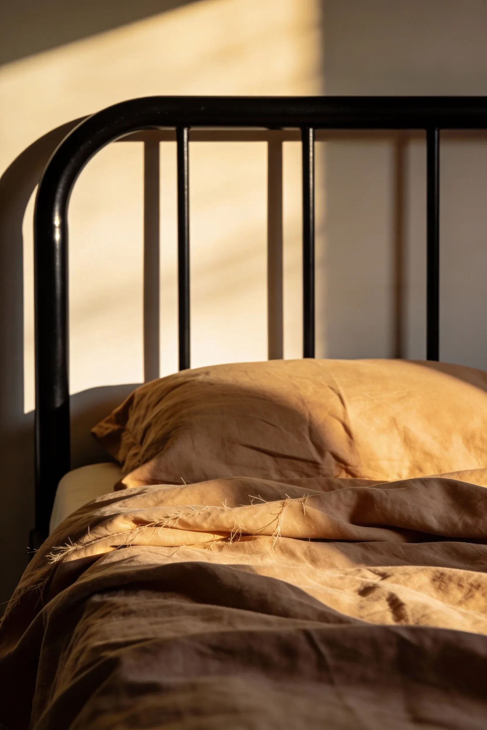 Black metal bed frame with tan linen bedding under warm natural lighting.