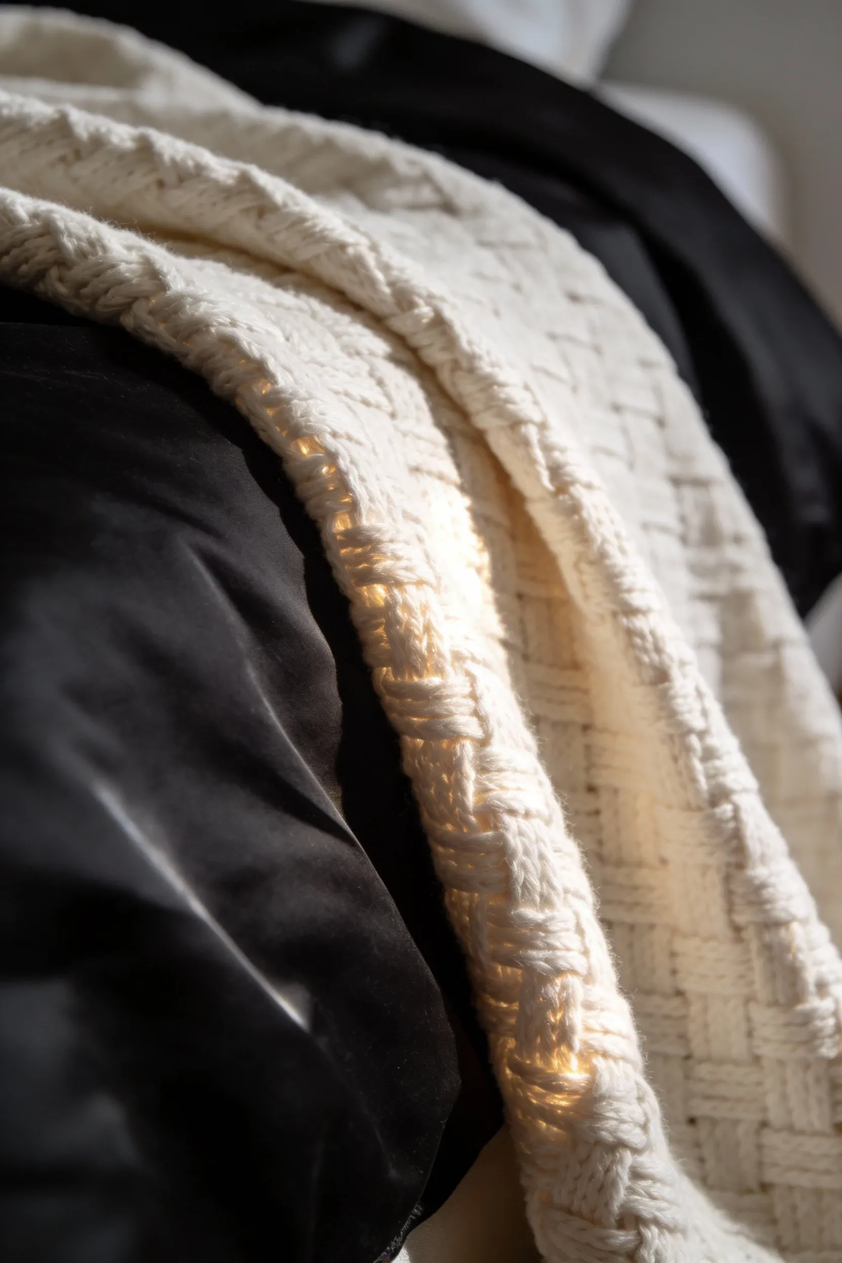 Ivory throw blanket draped across a black duvet with soft ambient lighting.