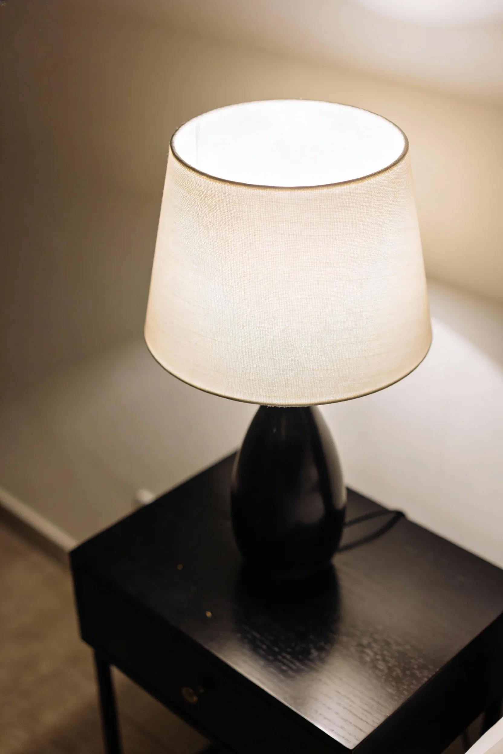 Black nightstand with a cream table lamp softly illuminating a modern bedroom.