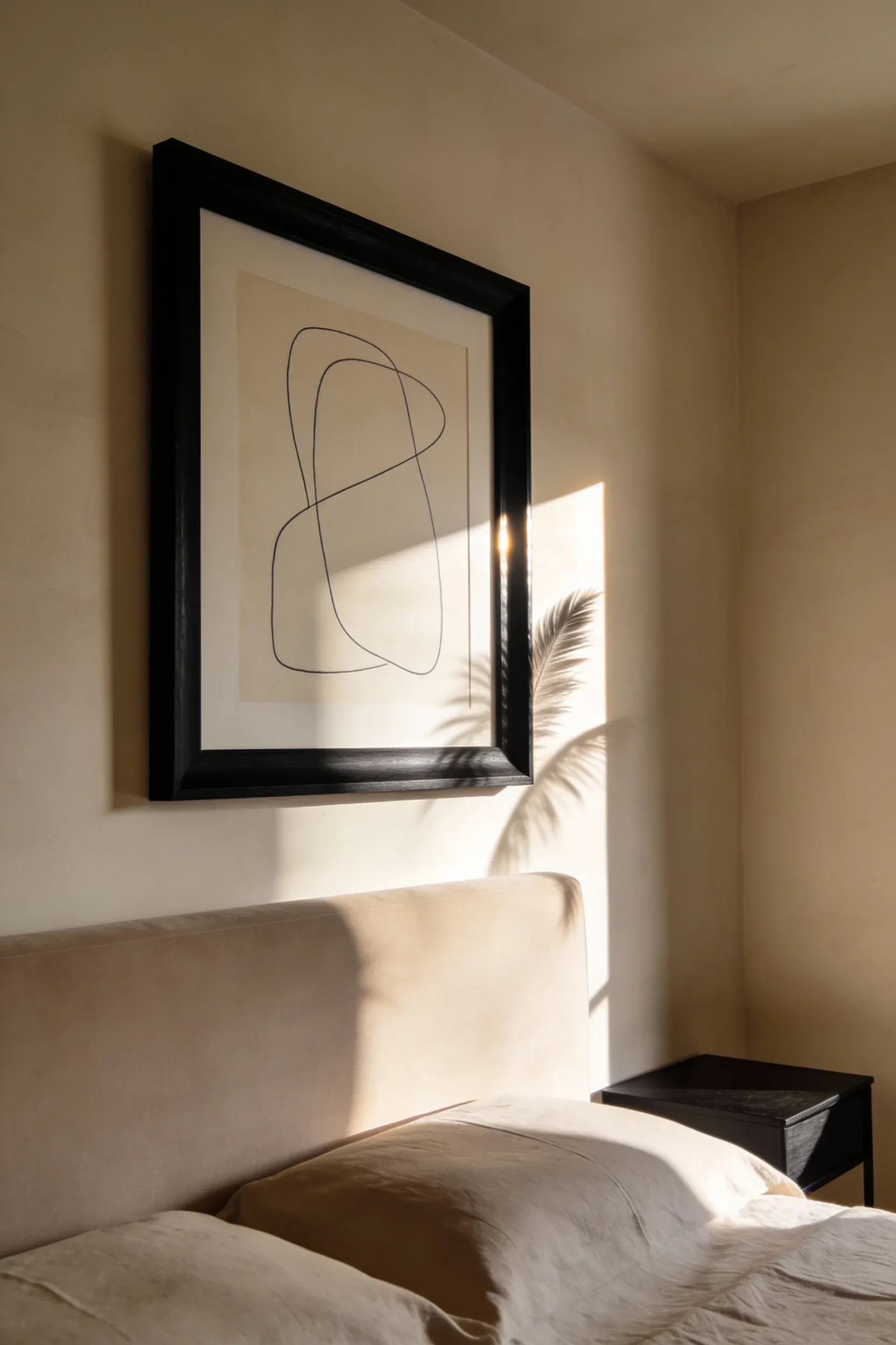 Black-framed minimalist artwork hanging on warm beige bedroom wall with soft natural lighting.