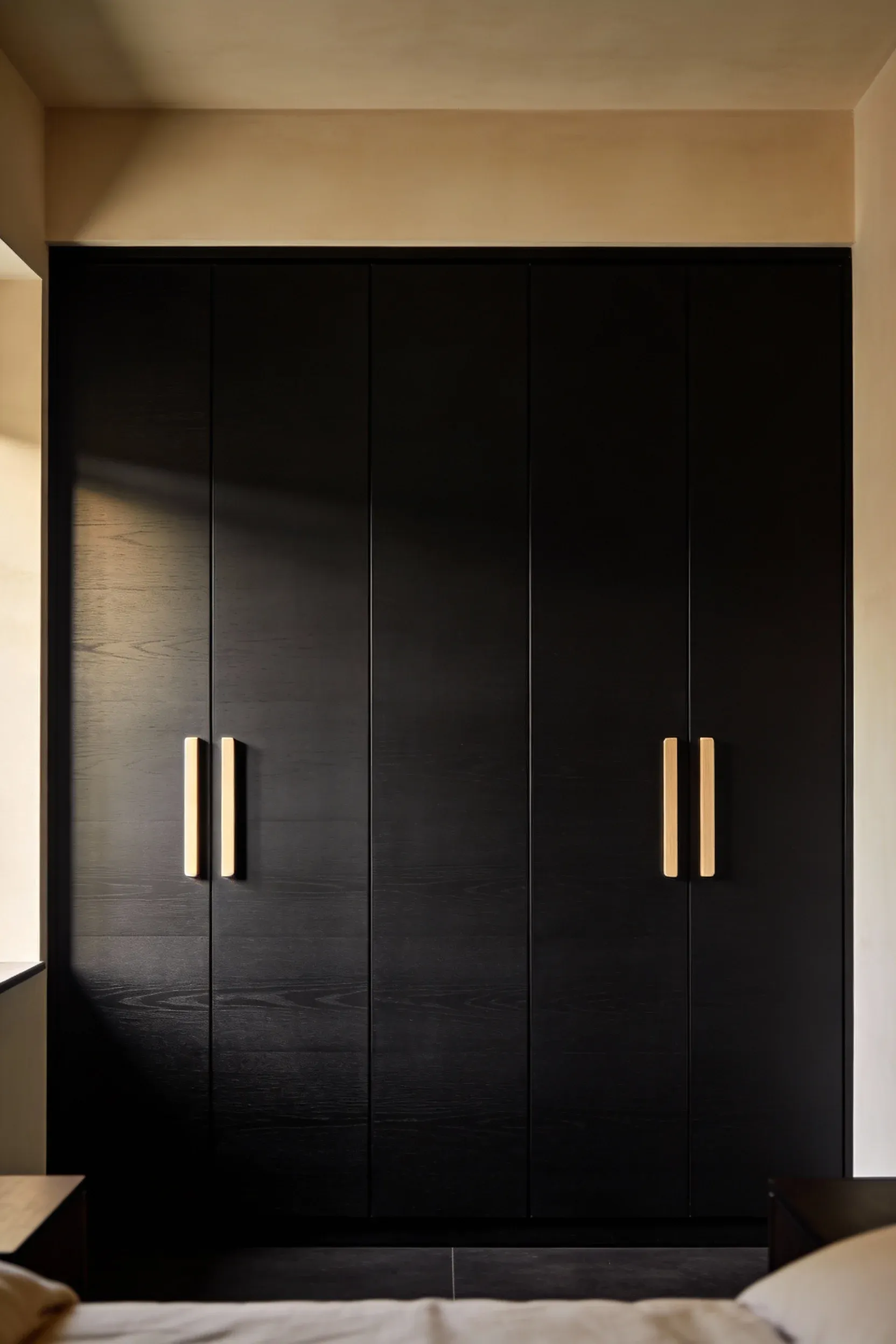 Matte black wardrobe with light wood handles in a calm beige bedroom.