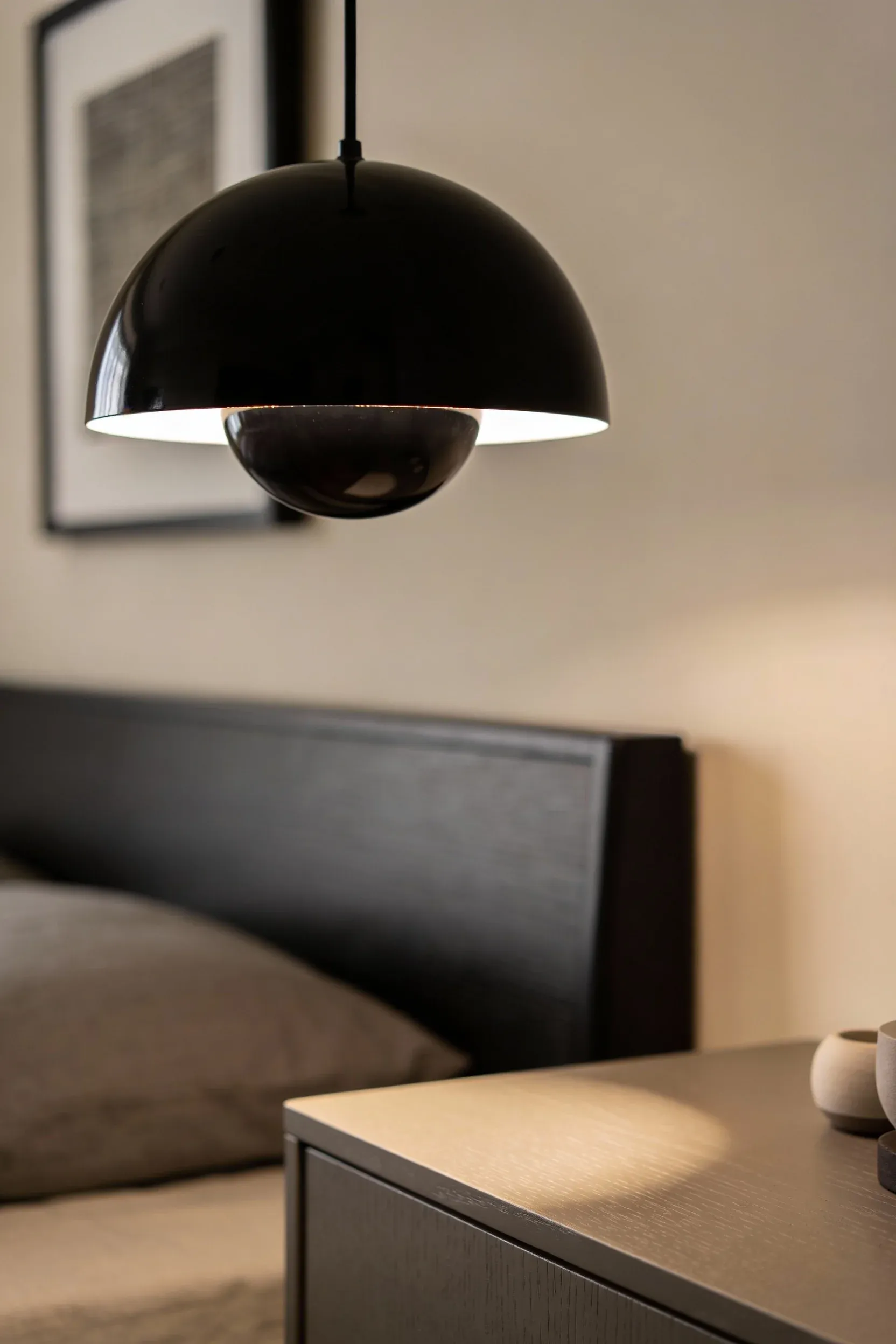 Black pendant light hanging above a taupe nightstand in a modern beige bedroom.