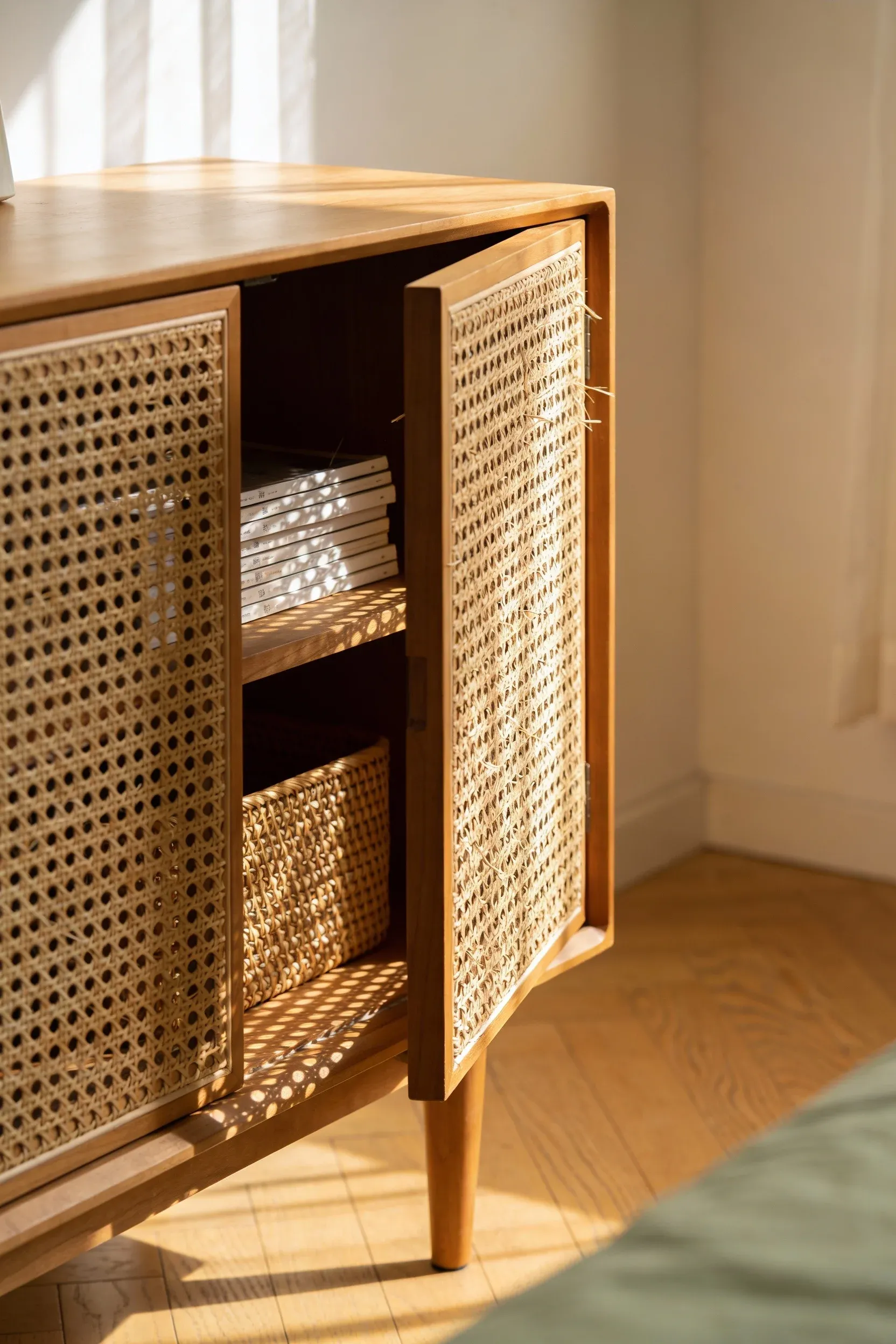 A rattan nightstand with open storage in a warm, airy natural bedroom.