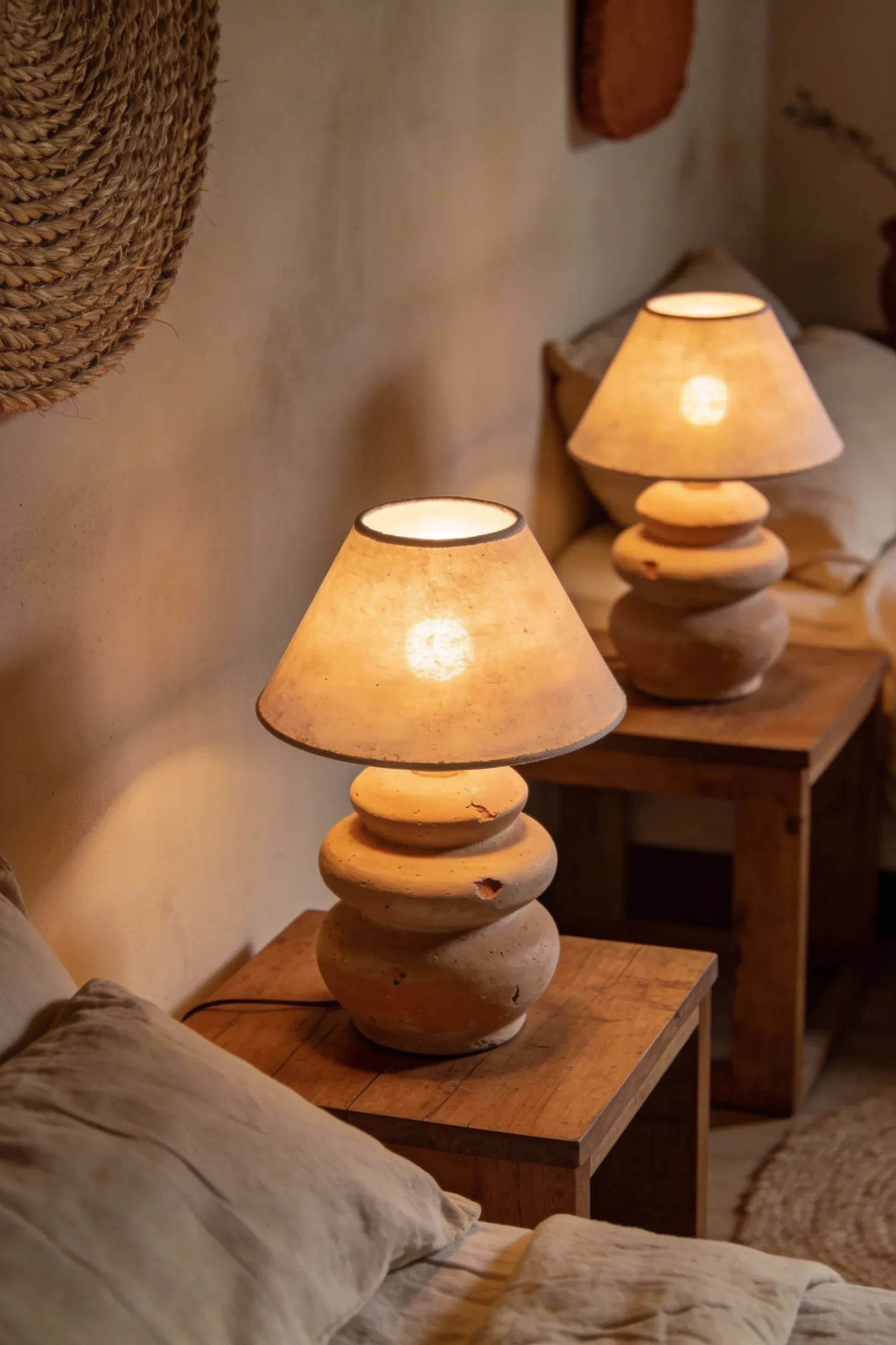 Stacked stoneware lamp glowing warmly on a wooden bedside table in a natural bedroom.