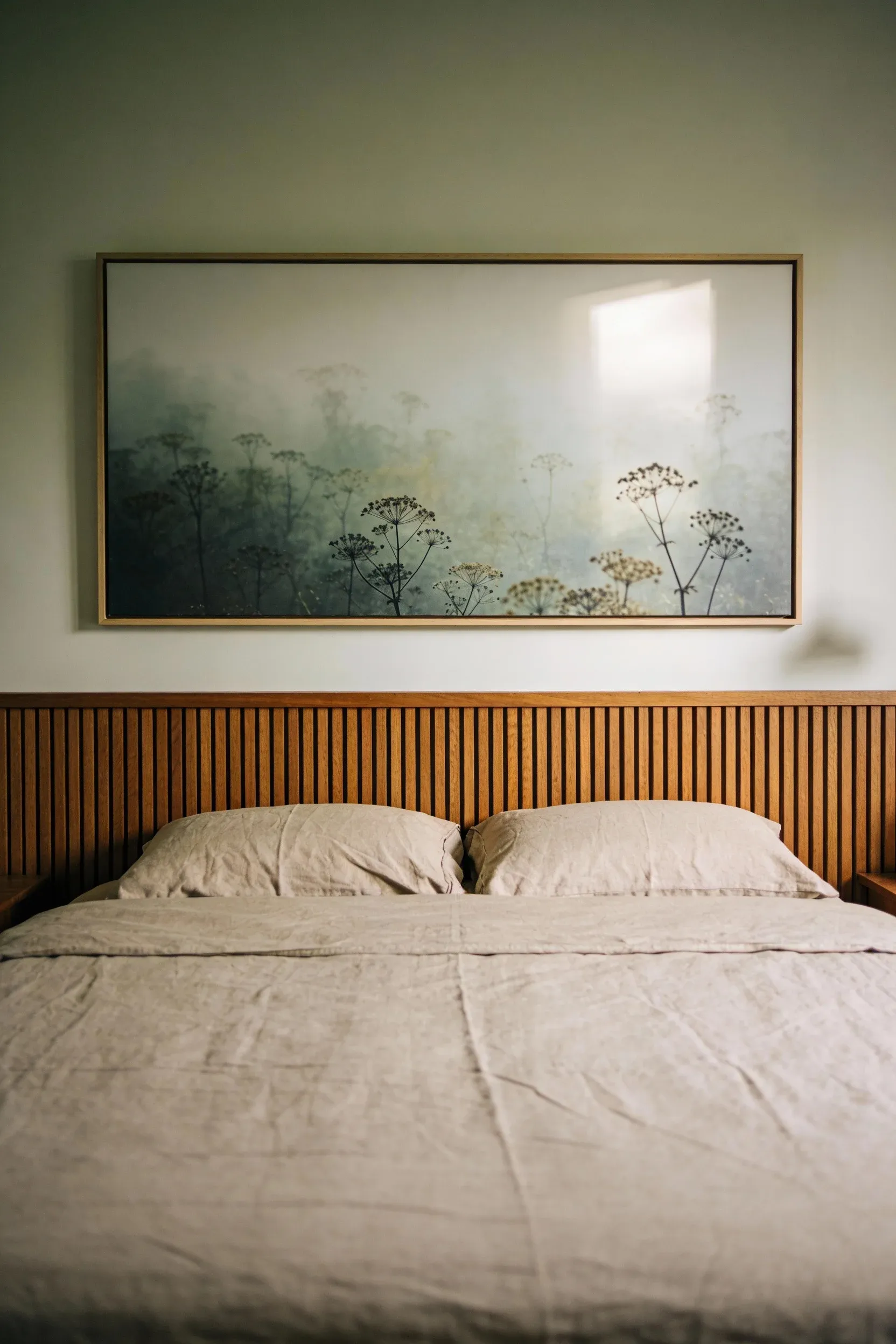 Large muted nature print hanging above a wooden bed in a warm natural bedroom.