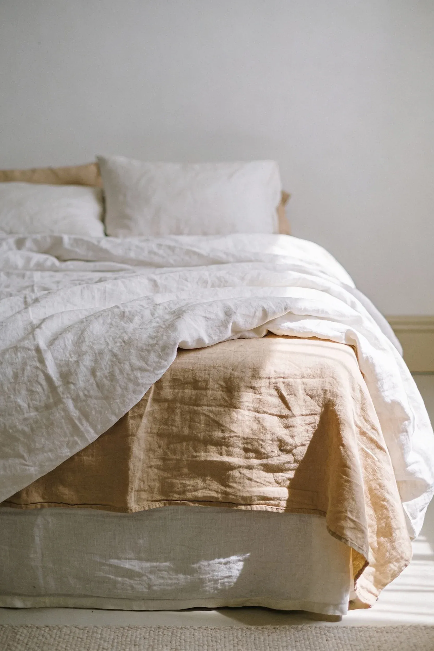 Bed styled with layered white and beige linen bedding in a soft, calming bedroom.