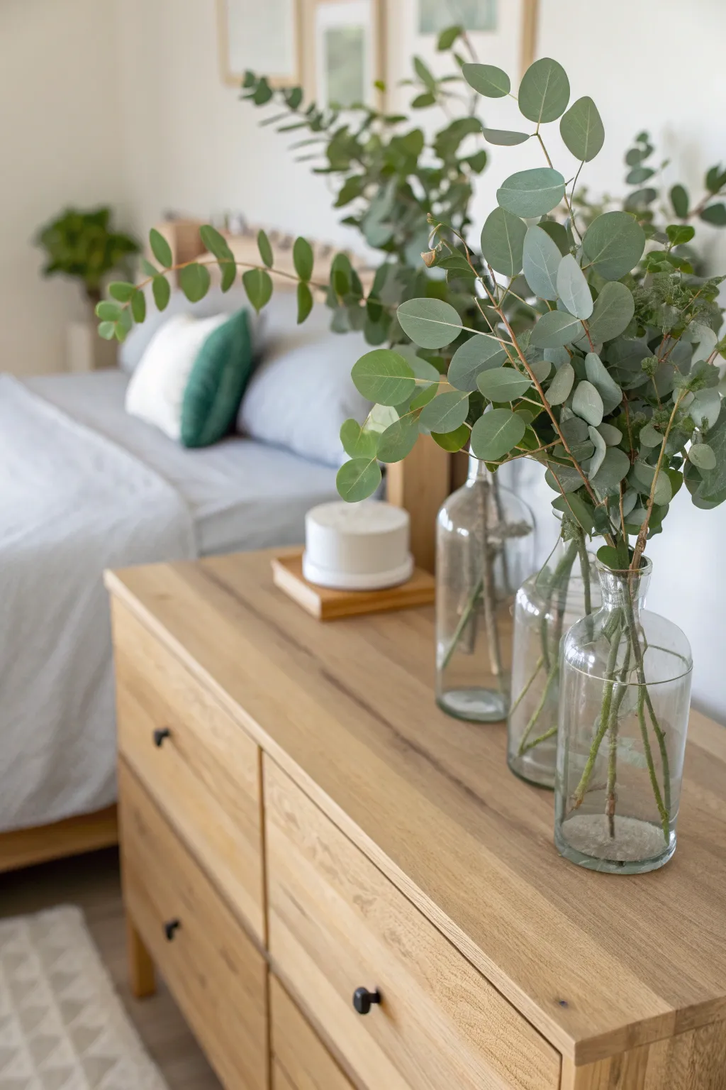 Fresh eucalyptus sprigs in clear glass vases on a wooden dresser in a bright green bedroom.