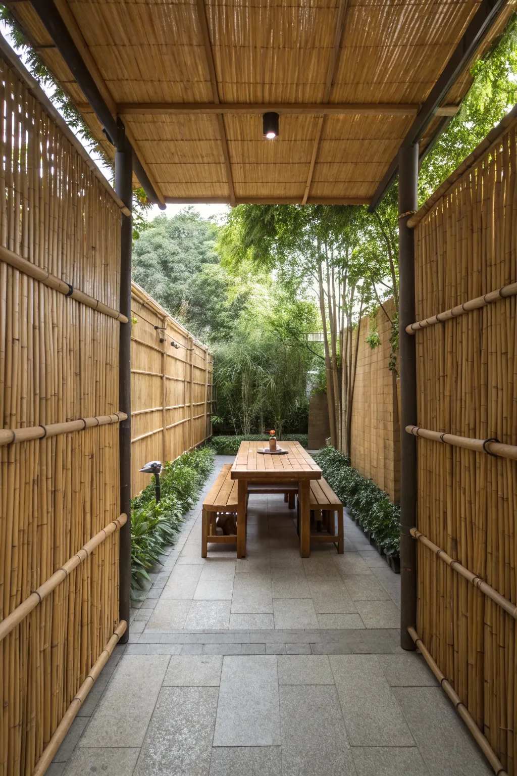 A private garden dining area surrounded by tall bamboo screens with a teak table on slate tiles.