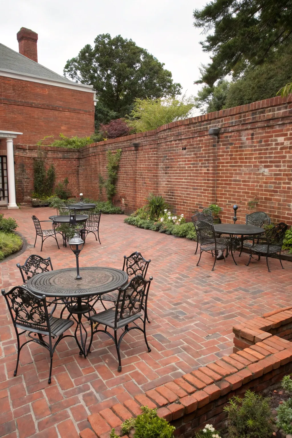 A red brick courtyard with a black wrought iron dining set and cream cushions.