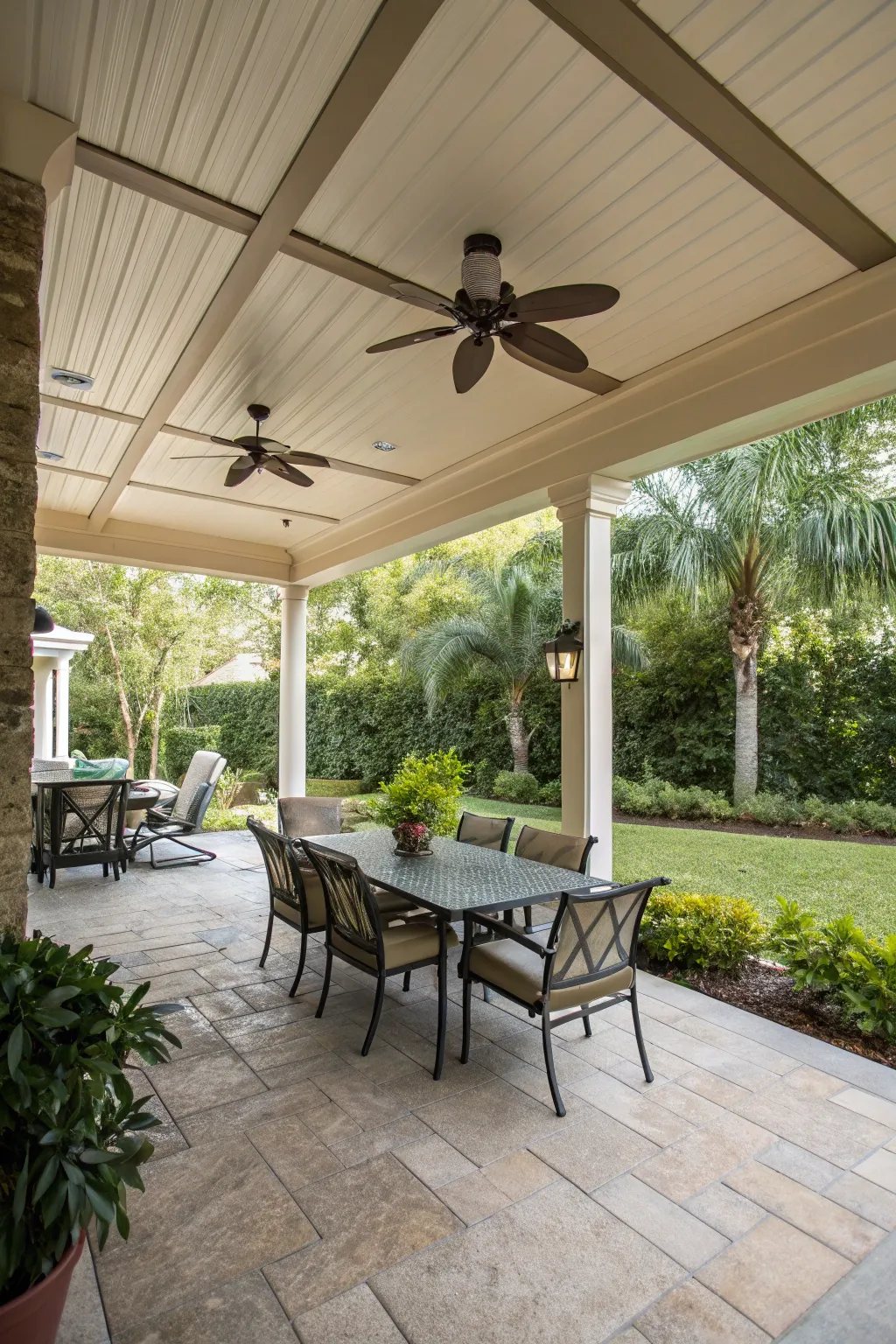 A covered wooden patio with a ceiling fan over a teak dining table set for a meal.