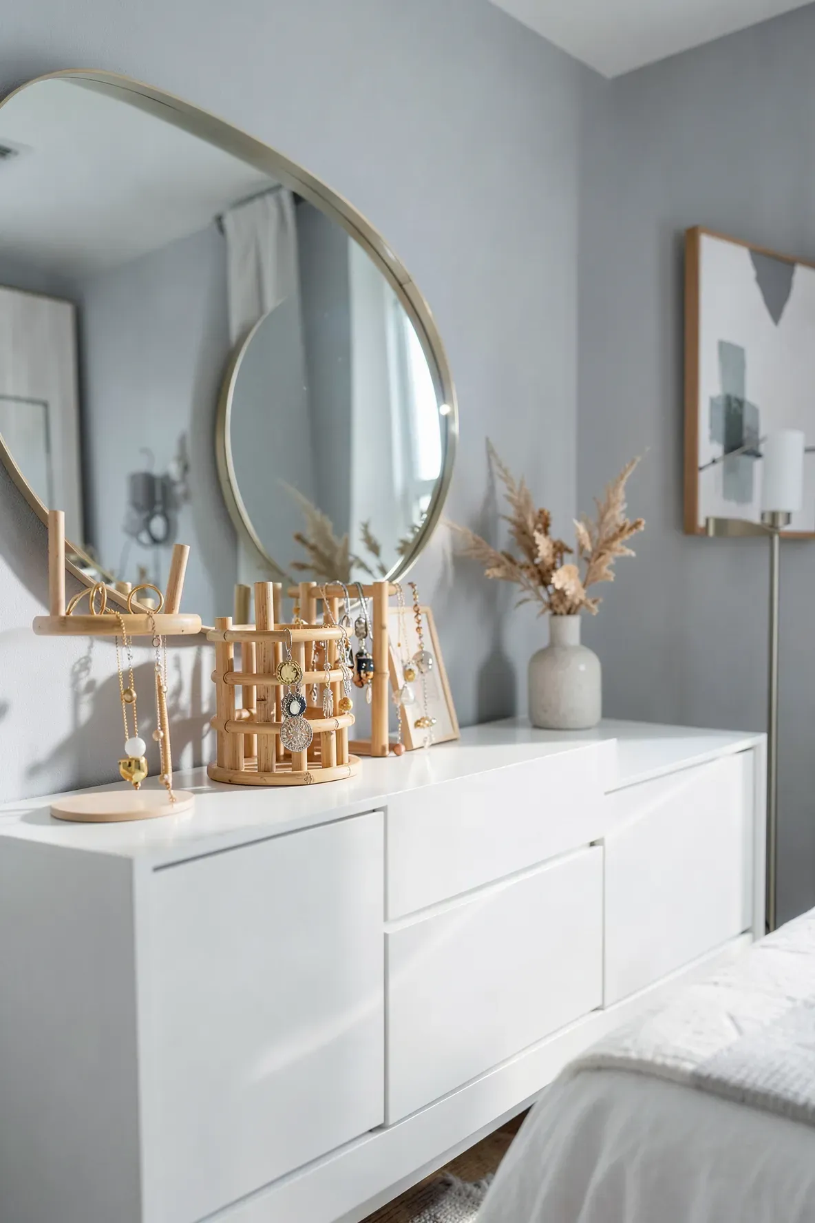 A bamboo jewelry organizer with necklaces and rings on a clean white dresser in a bedroom.
