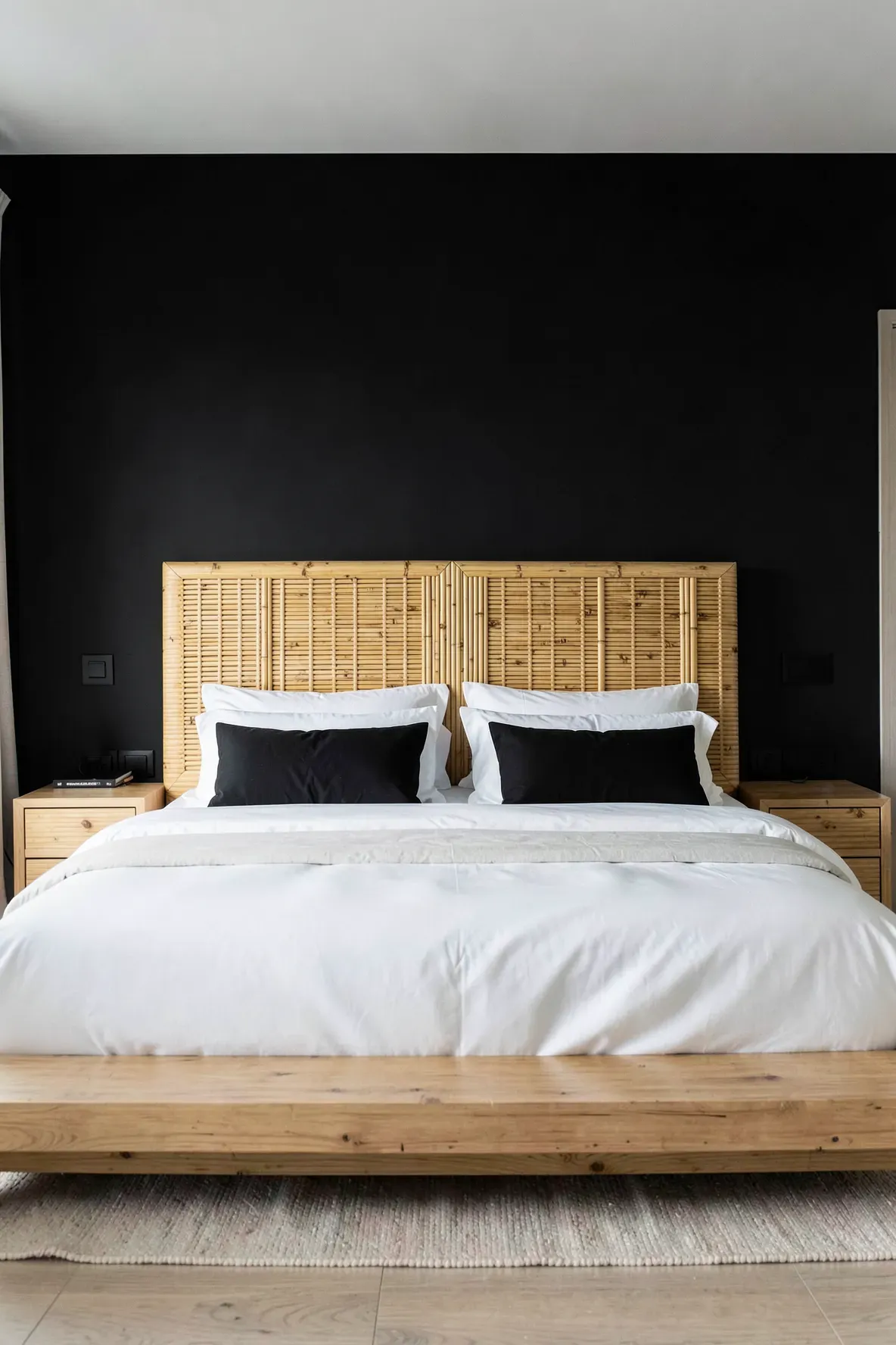 A matte black bedroom wall highlighting a light-toned bamboo headboard with natural wood grain.