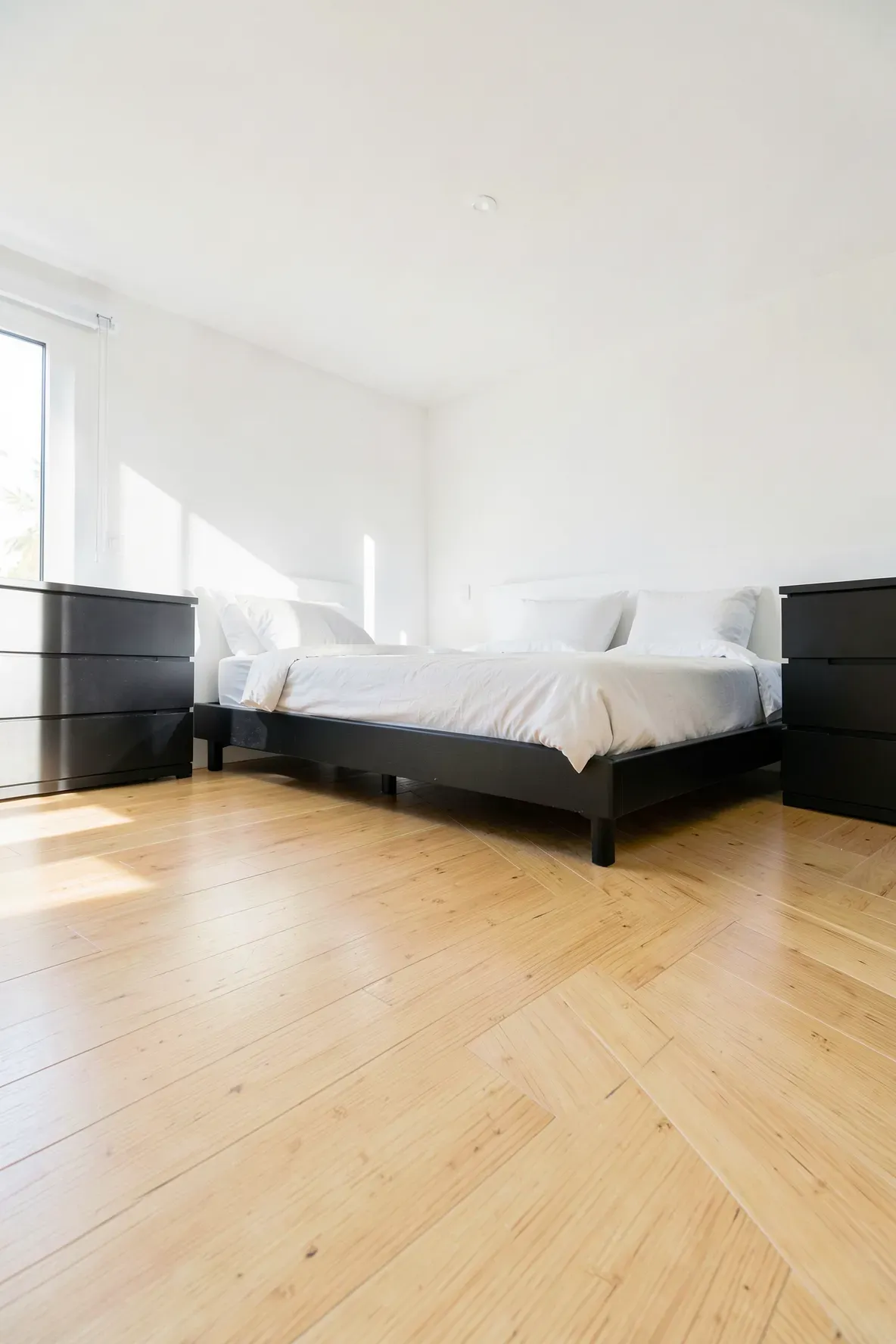 Light-colored bamboo wood flooring in a bedroom with black furniture and white walls.