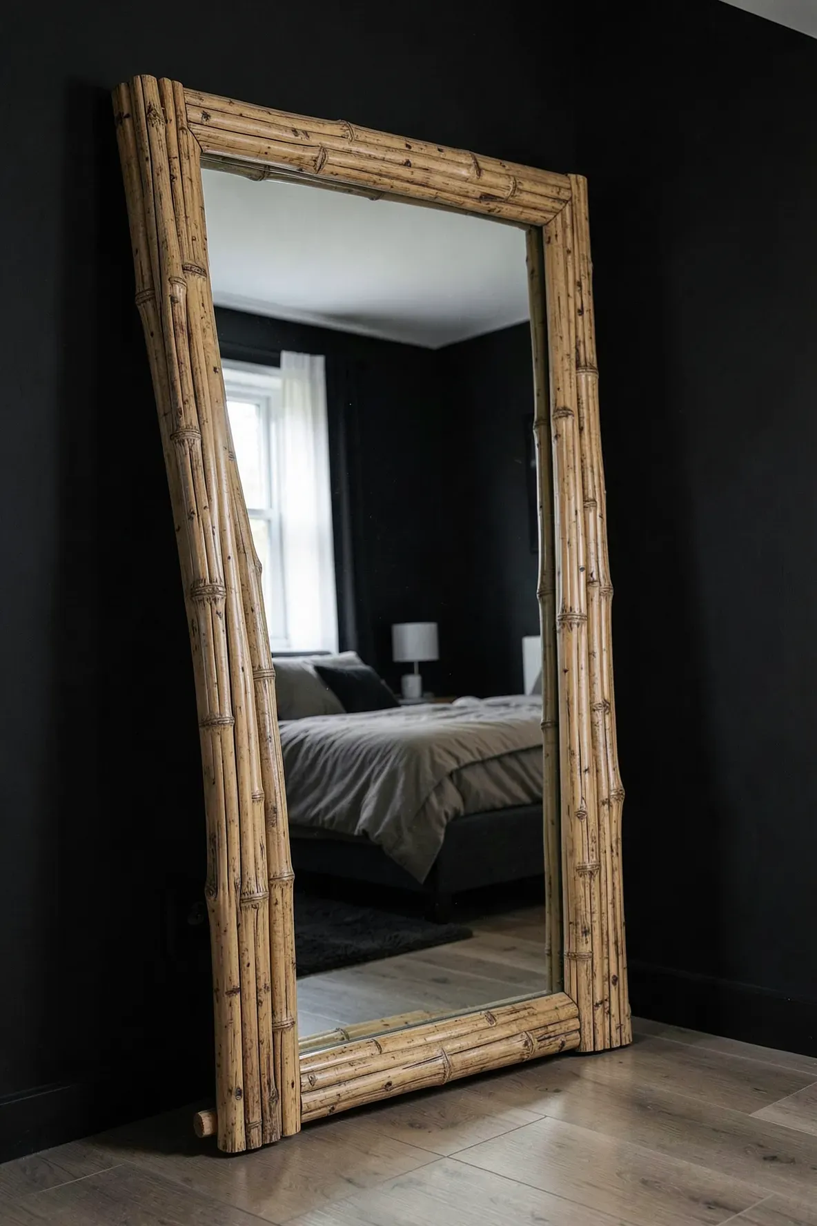 A large mirror with a thick bamboo frame leaning against a dark black bedroom wall.