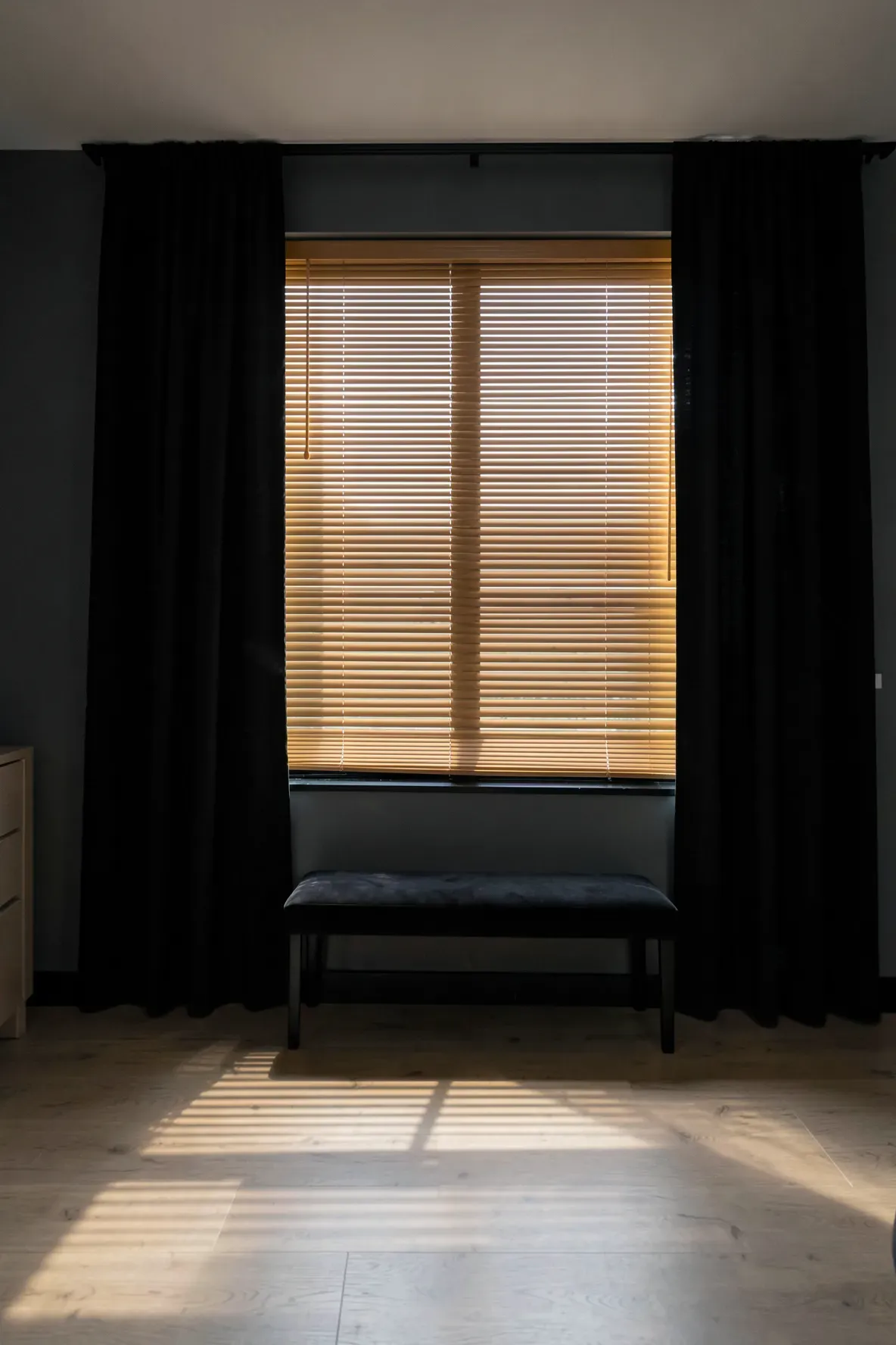 Polished bamboo window blinds filtering light into a moody bedroom with black accents.