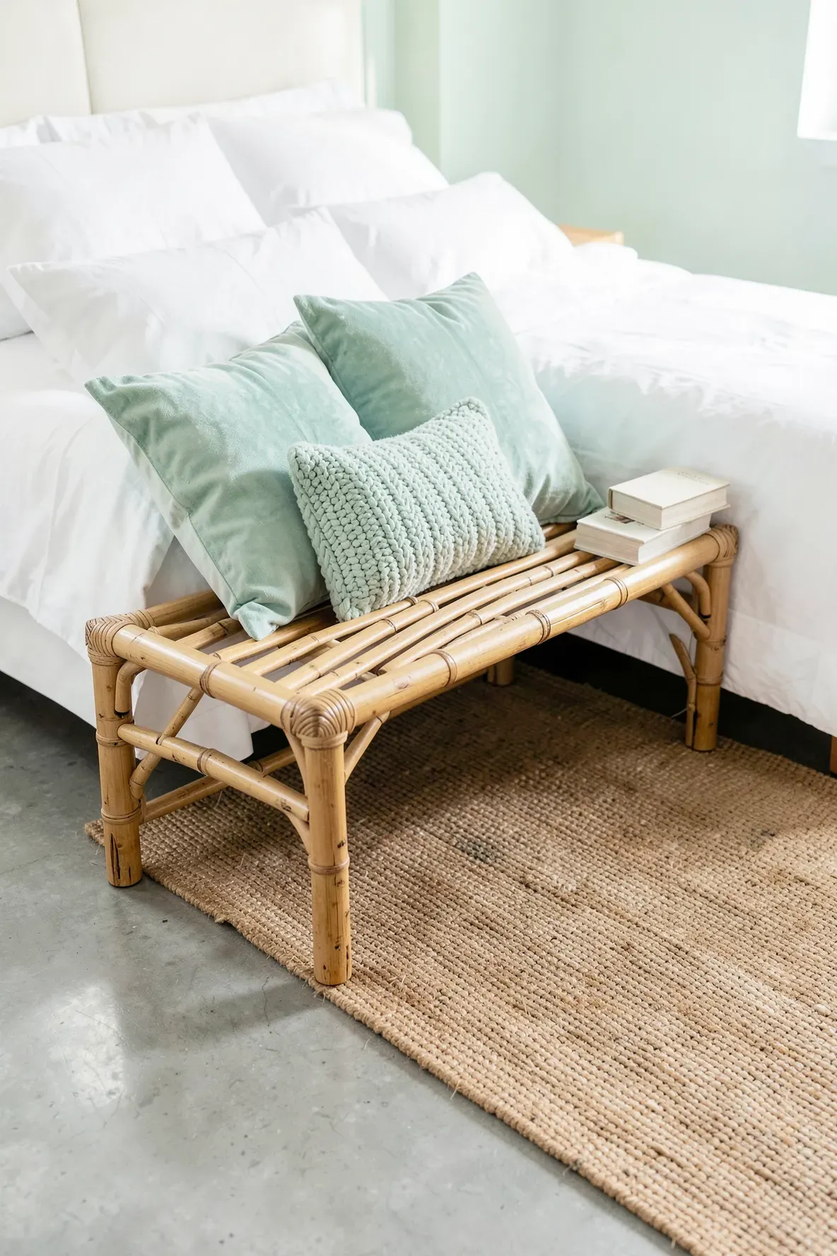 Soft mint green throw pillows resting on a natural bamboo bench at the foot of a bed.