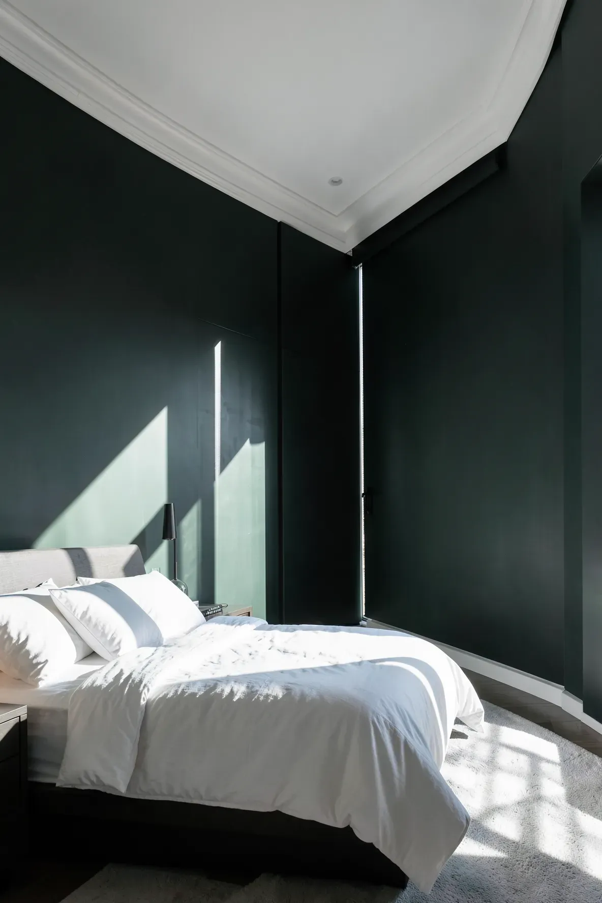 A dark charcoal-green bedroom wall transformed by bright sunlight from a large window.
