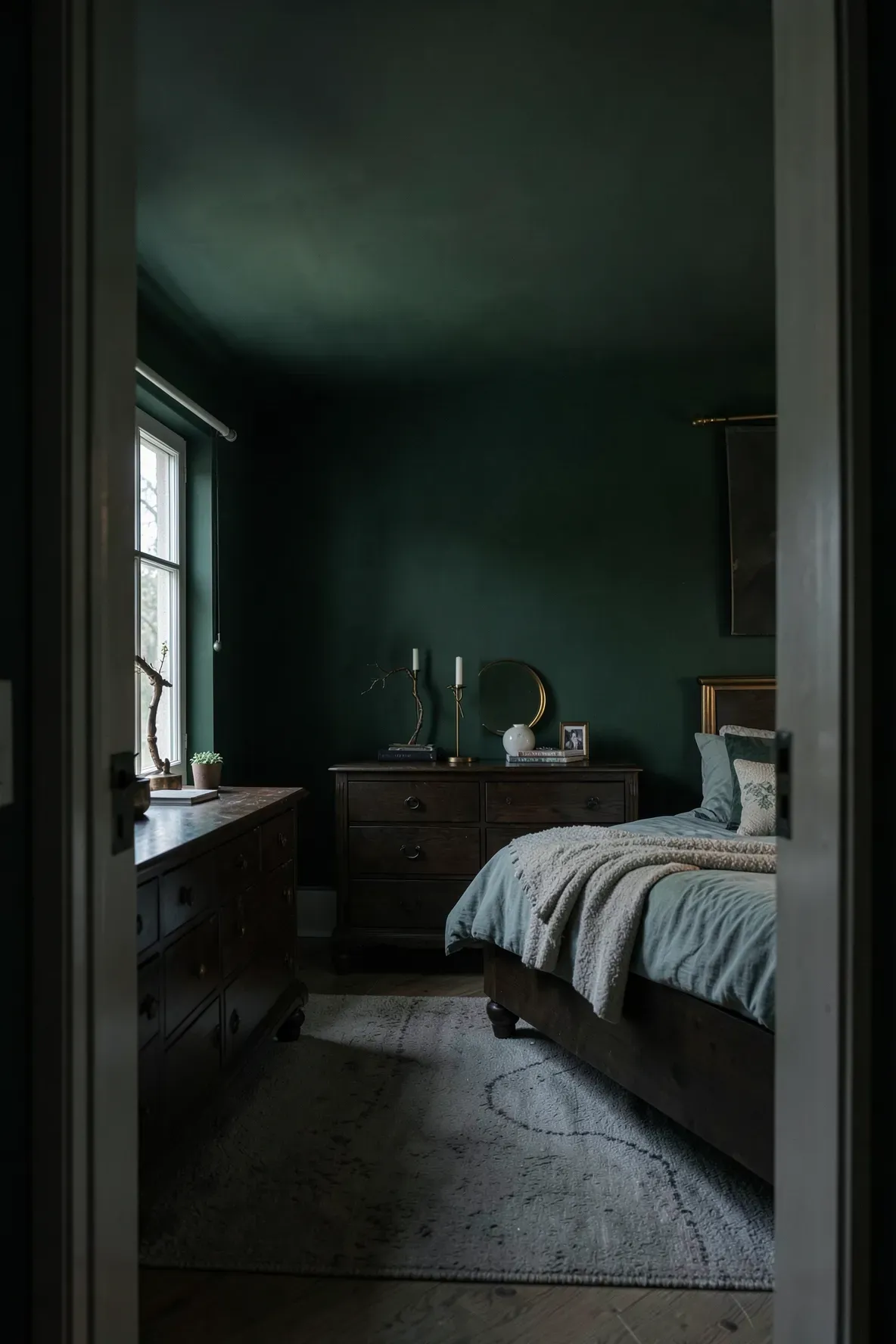 A bedroom with deep forest green matte walls, dark wood furniture, and moody natural lighting.