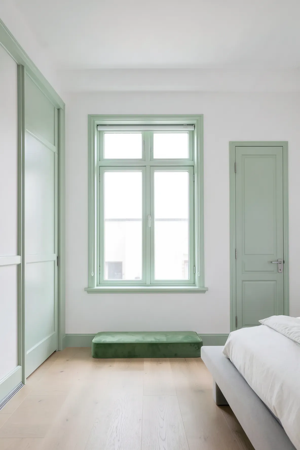 Pale celadon green painted window trim and door frames in a bright white bedroom.