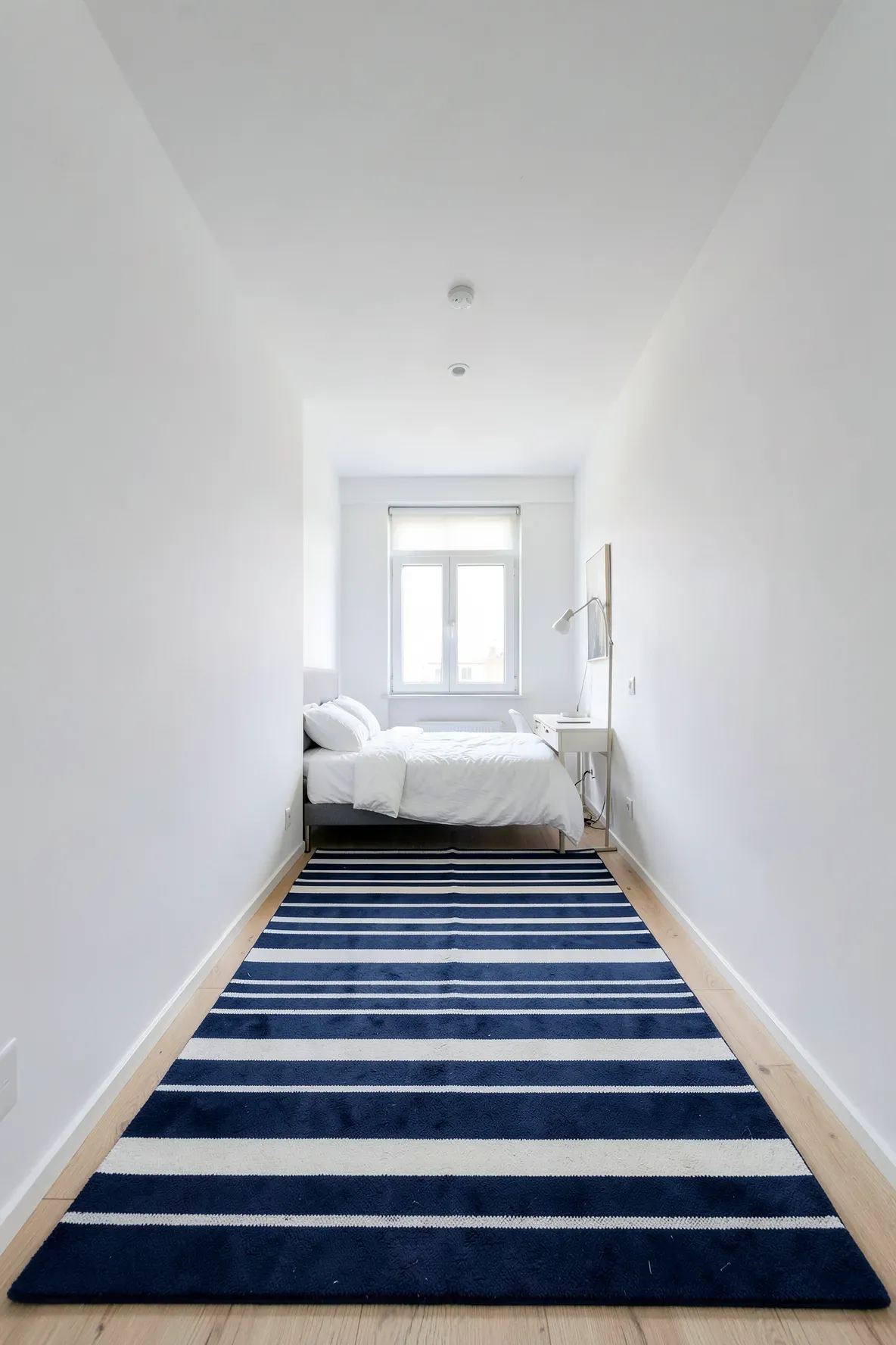A horizontal striped rug used to visually widen a narrow bedroom space.