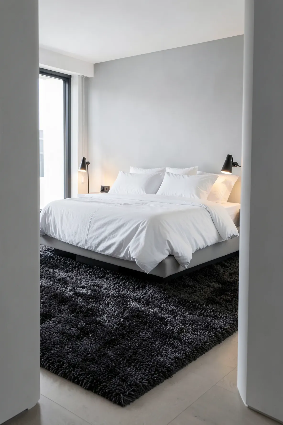 A dark charcoal rug provides a bold contrast to white bedding in a bright, modern minimalist bedroom.