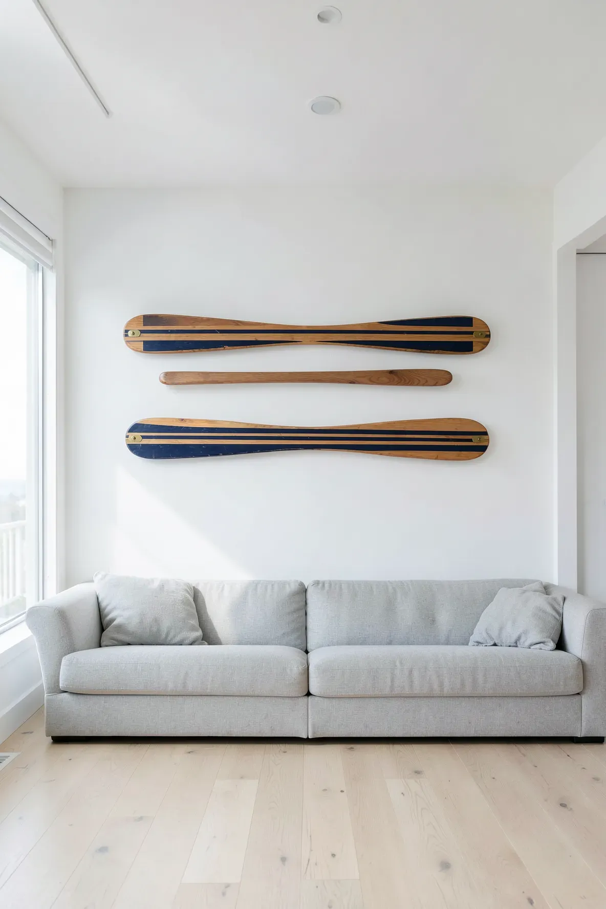 Two wooden oars with blue stripes are mounted horizontally on a white wall in a beachy room.