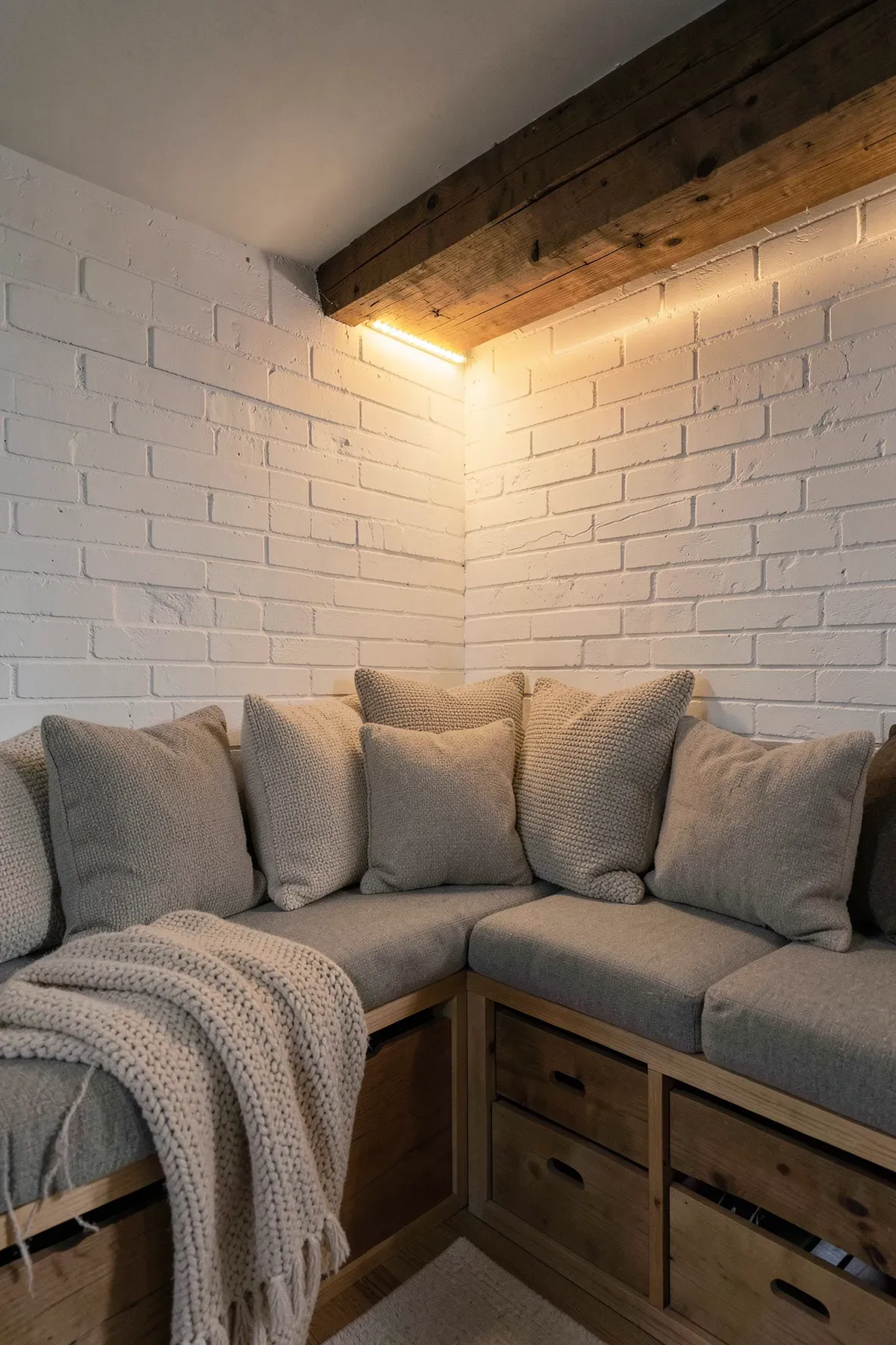 A cozy basement reading corner with built-in wooden bins and a large pile of soft knit pillows.